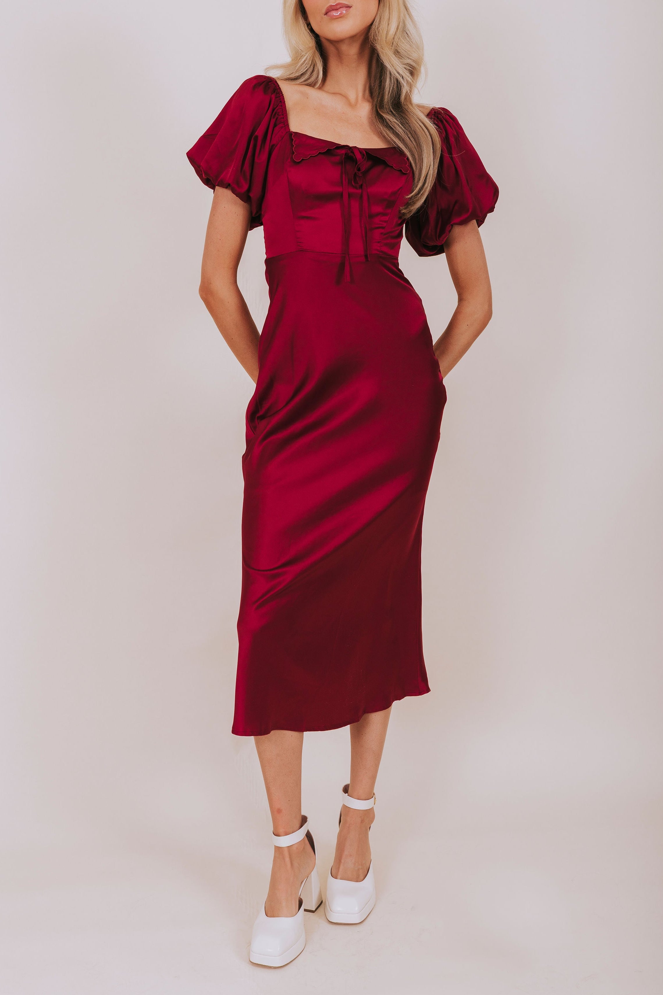 Woman wearing a burgundy dress with puff sleeves on a plain background
