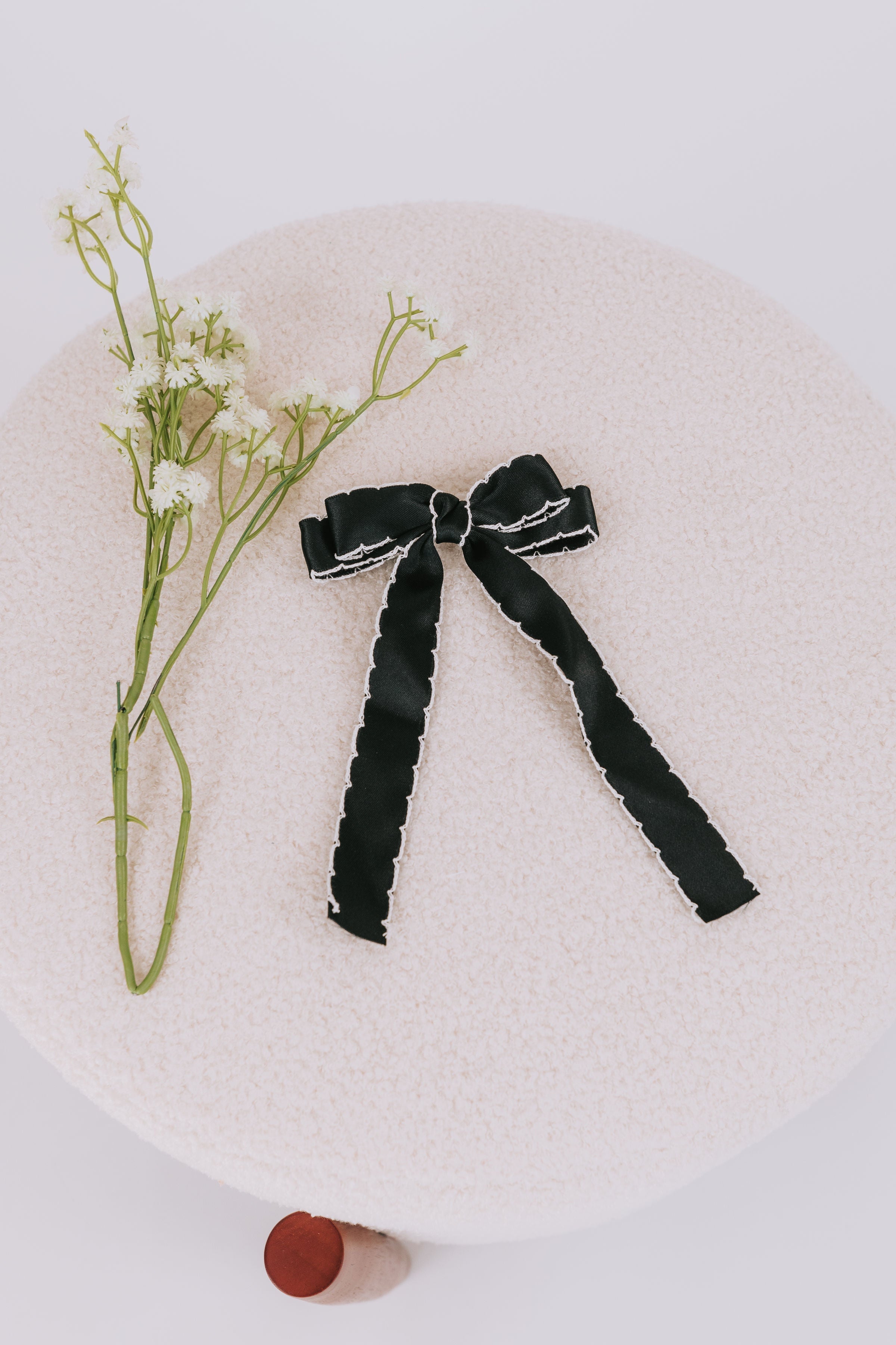 A black bow with white trim placed on a beige surface, accompanied by a sprig of flowers.