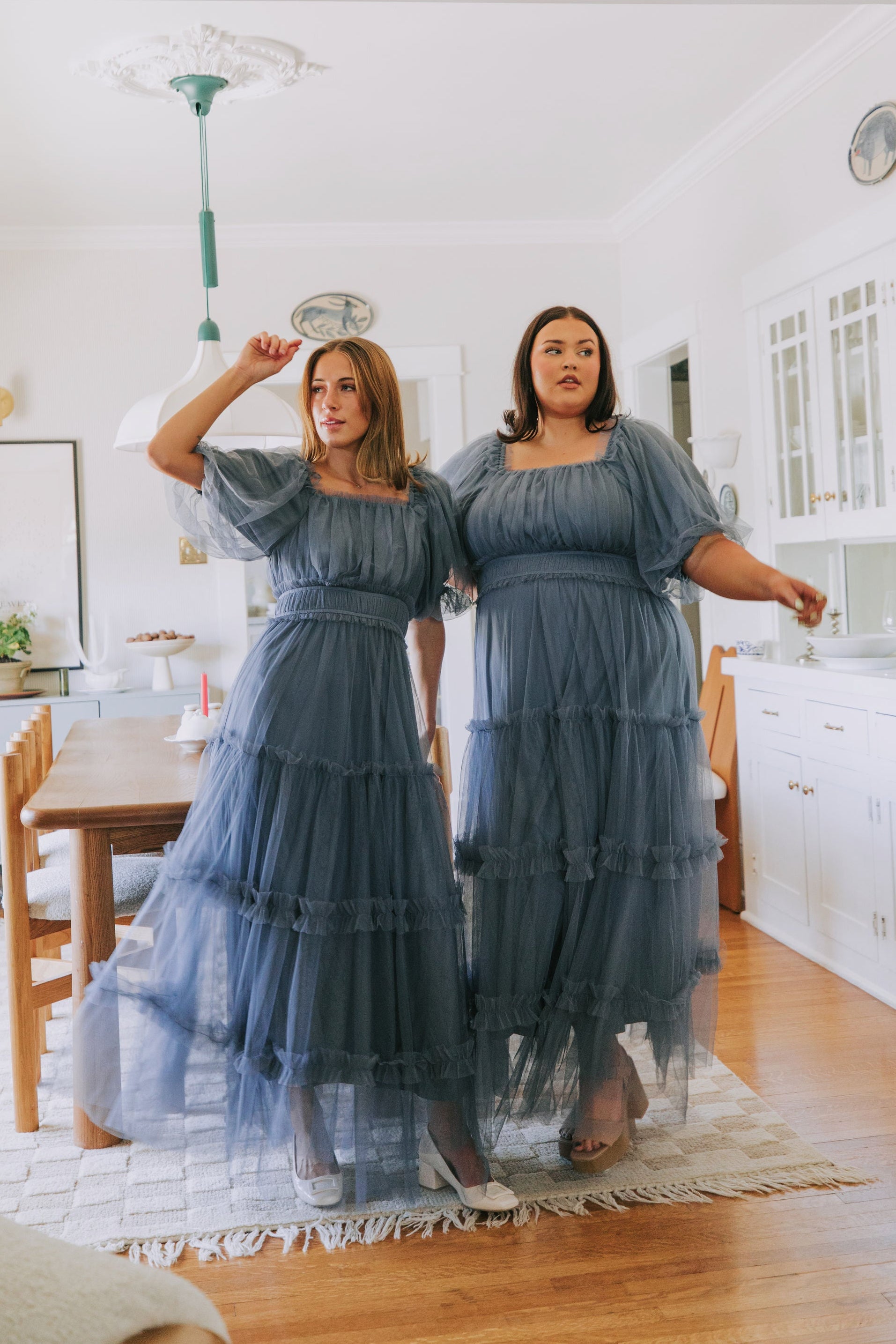Woman trying on a blue dress in a kitchen.