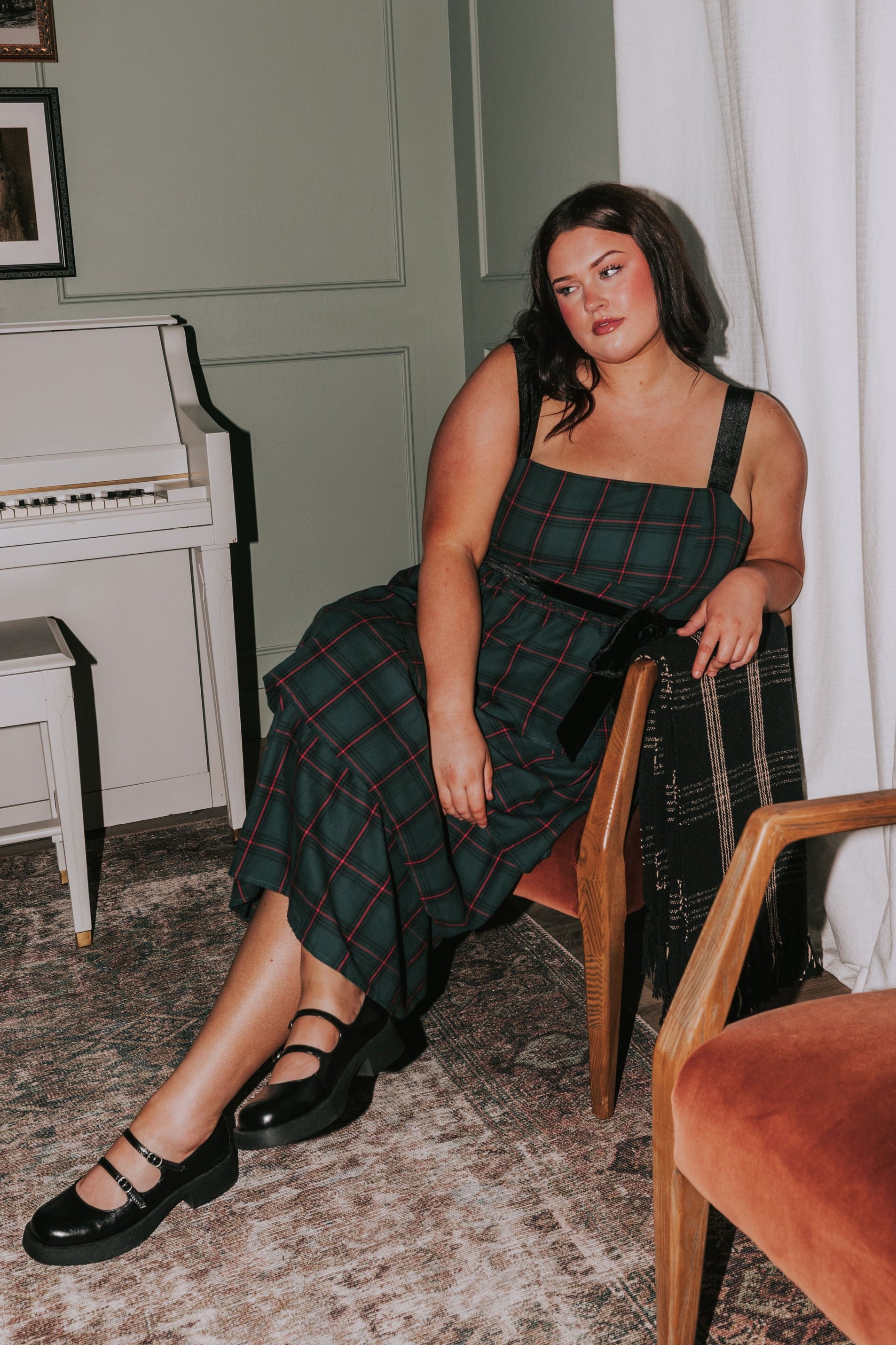 Woman in a plaid dress sitting in a room with a piano and curtains.