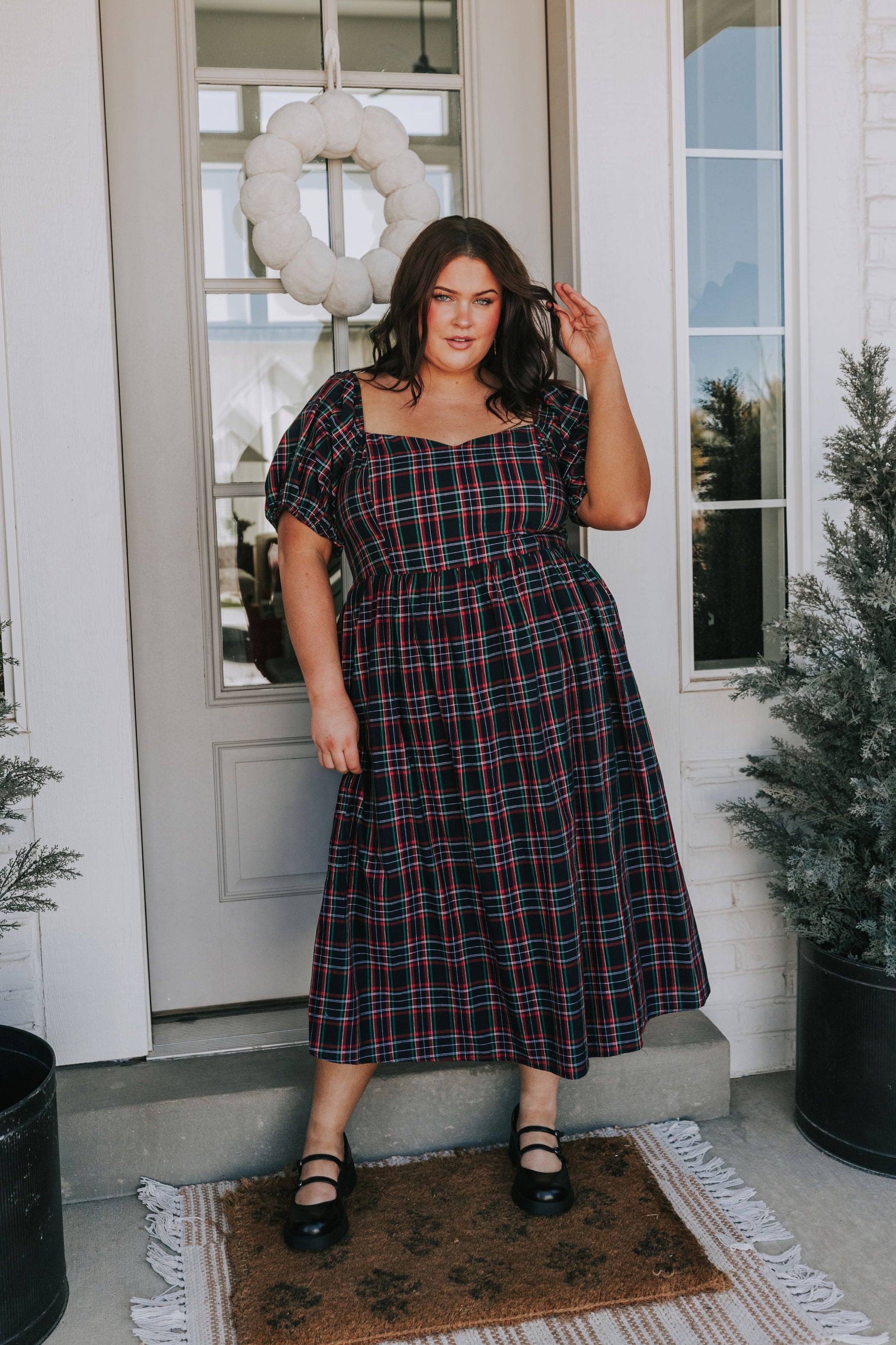 Woman in a plaid dress standing on a porch with decorative elements.