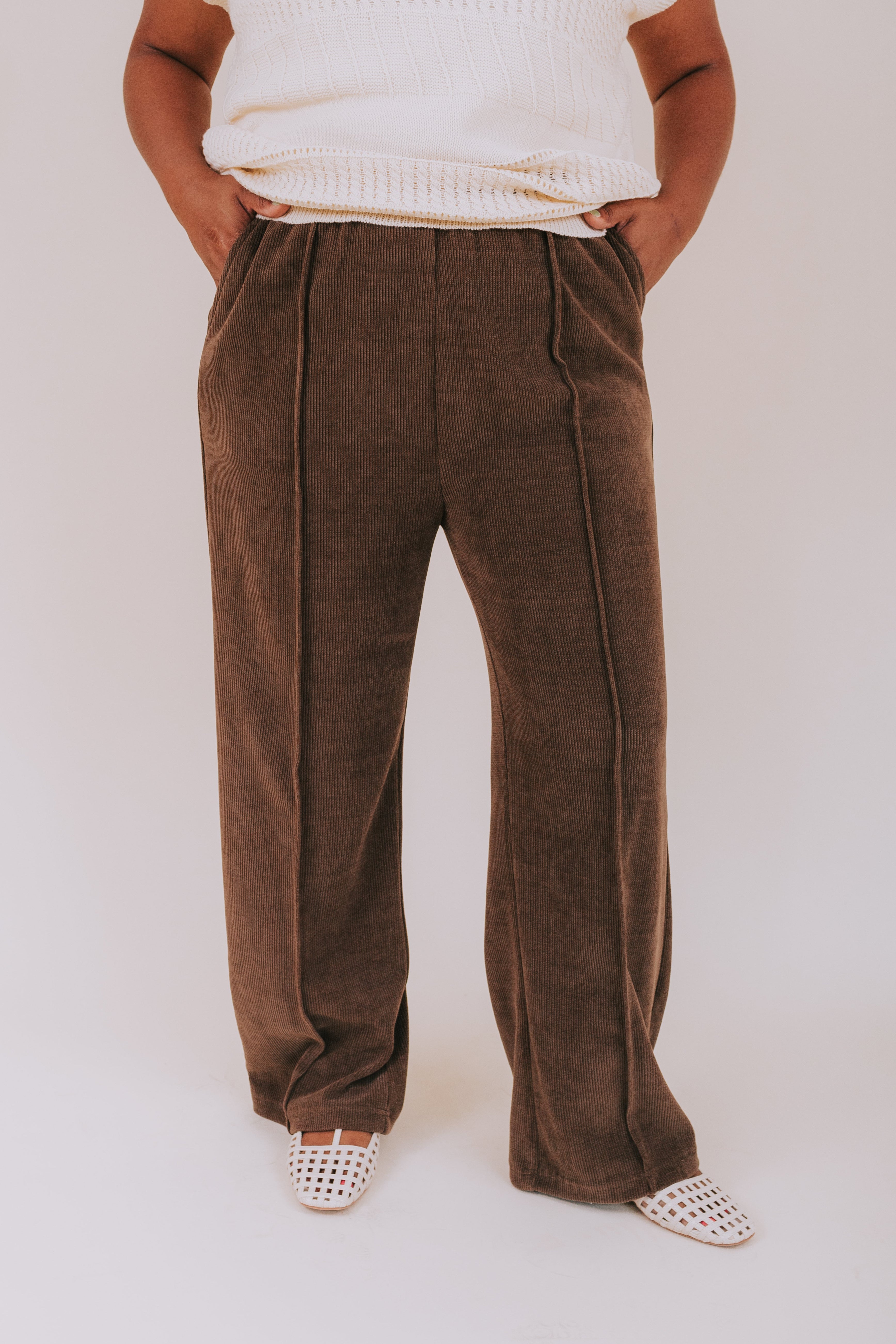 Person wearing brown corduroy pants and a white top against a plain background