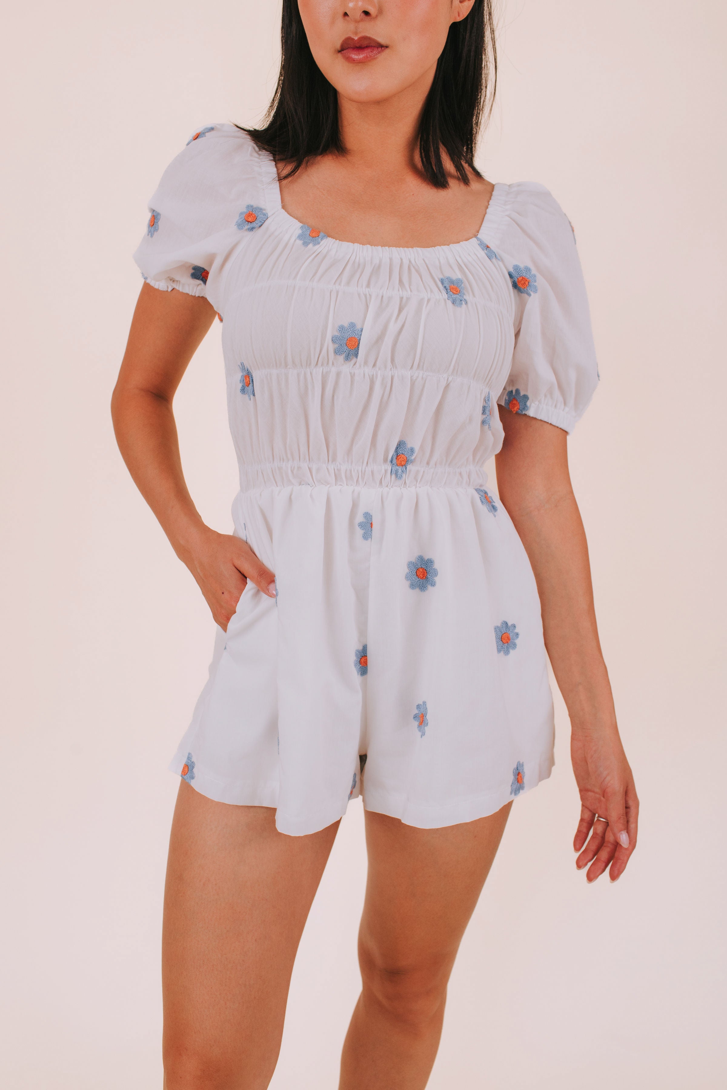 Woman wearing a white romper with blue daisies against a plain background