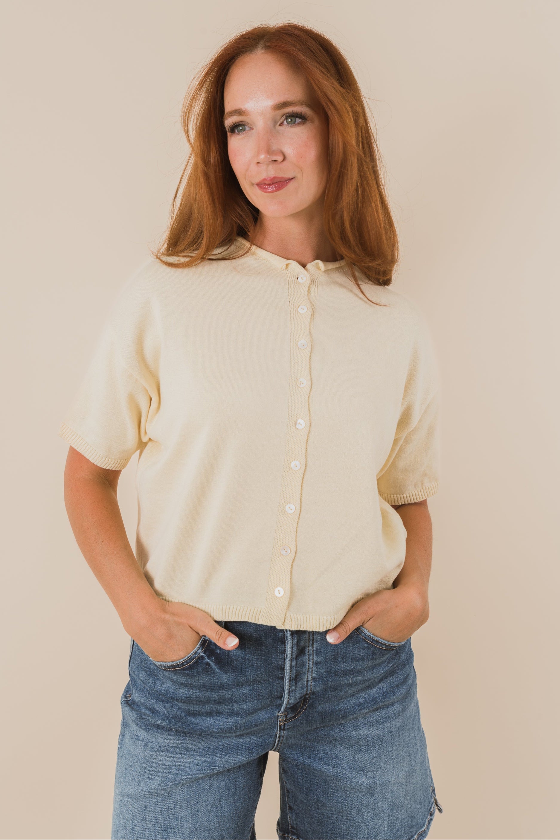 Woman wearing a pale yellow button-up shirt and blue jeans against a plain background