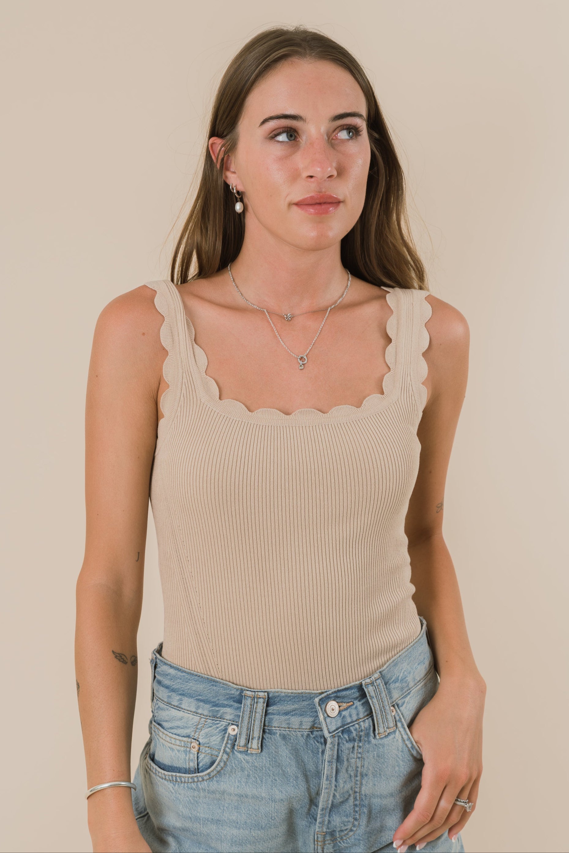 Woman wearing a beige tank top and blue jeans against a plain background