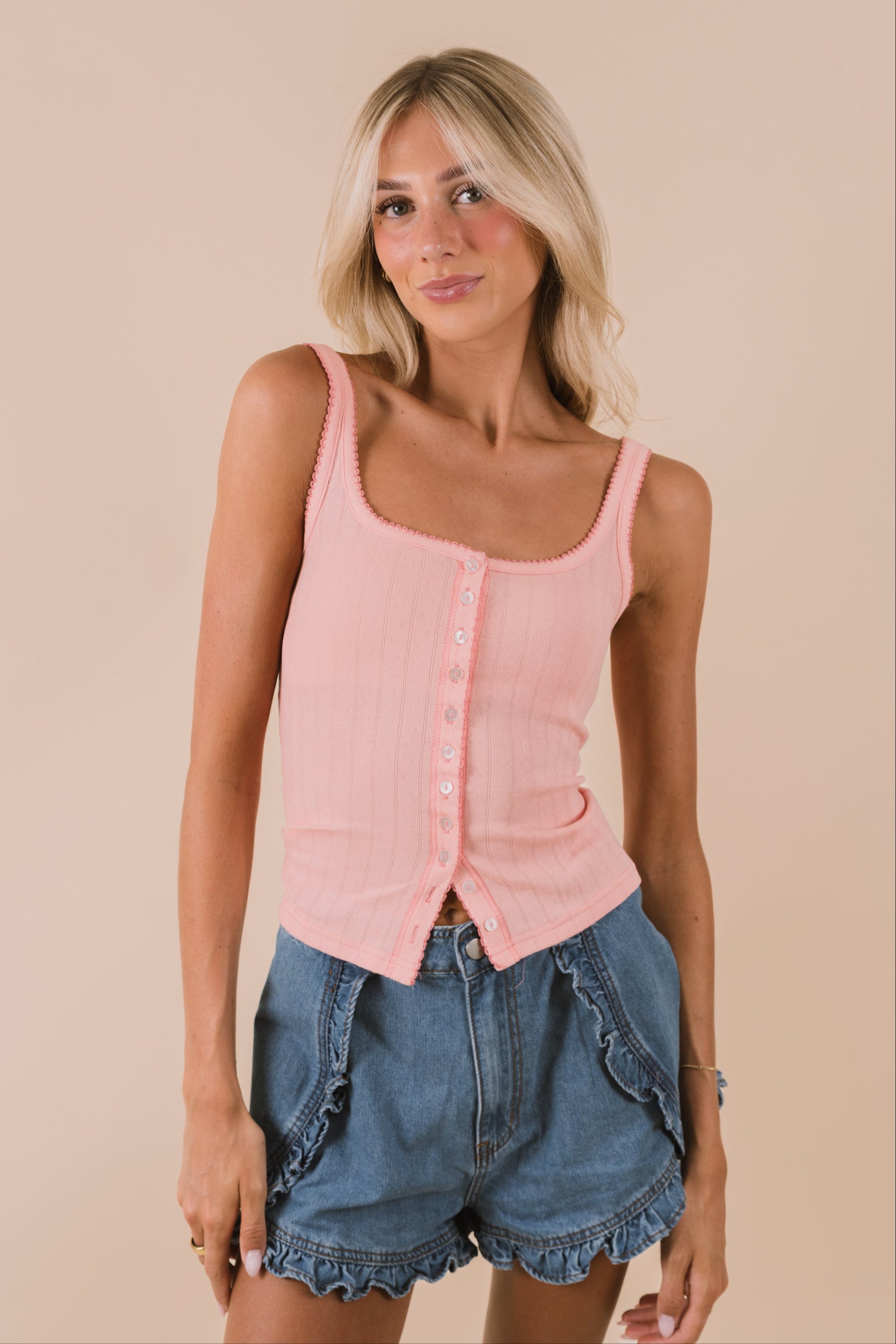 Woman wearing a free people pink tank top and denim shorts on a beige background