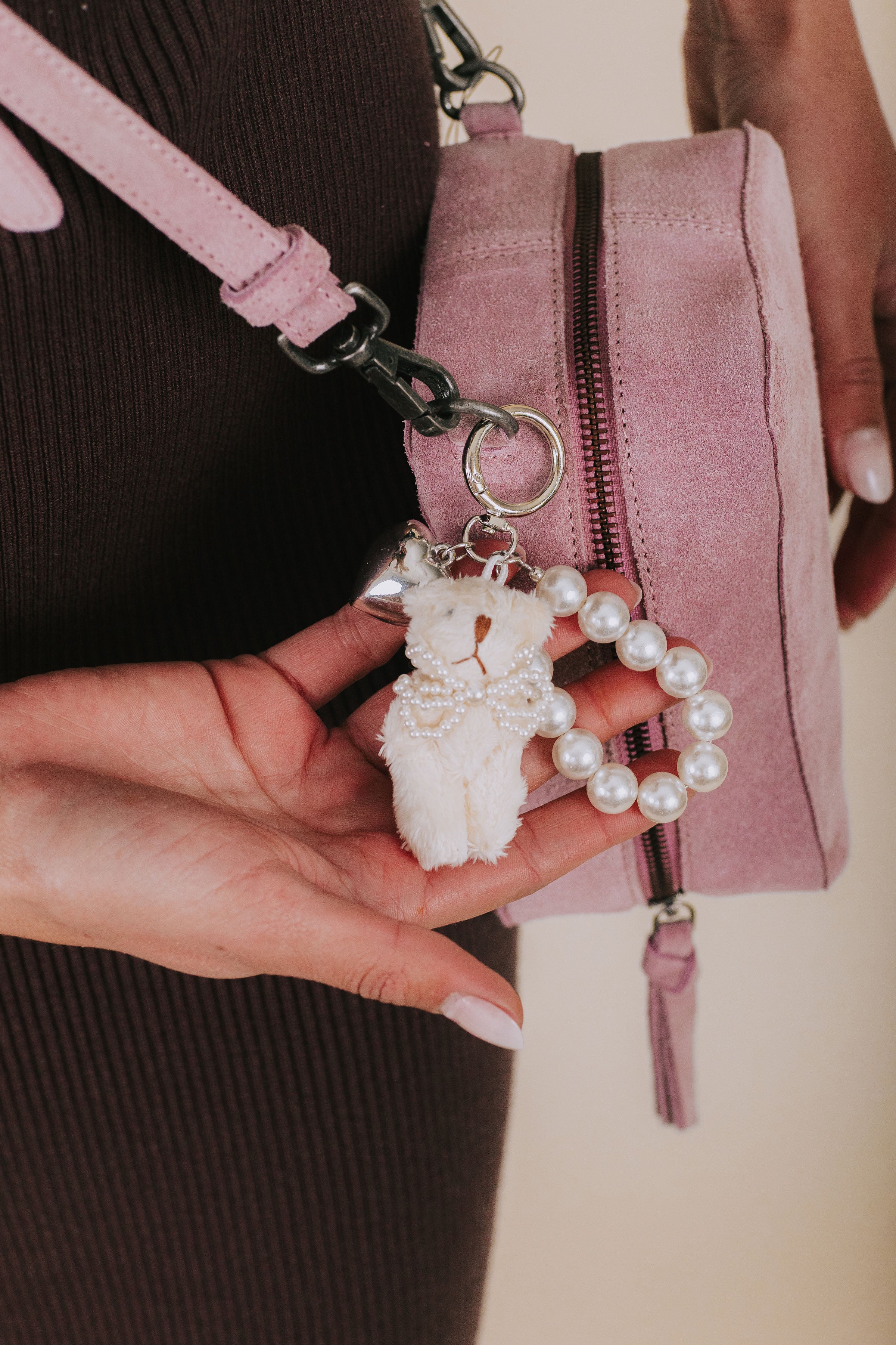 Pink handbag with a decorative keychain featuring a white bear and pearls