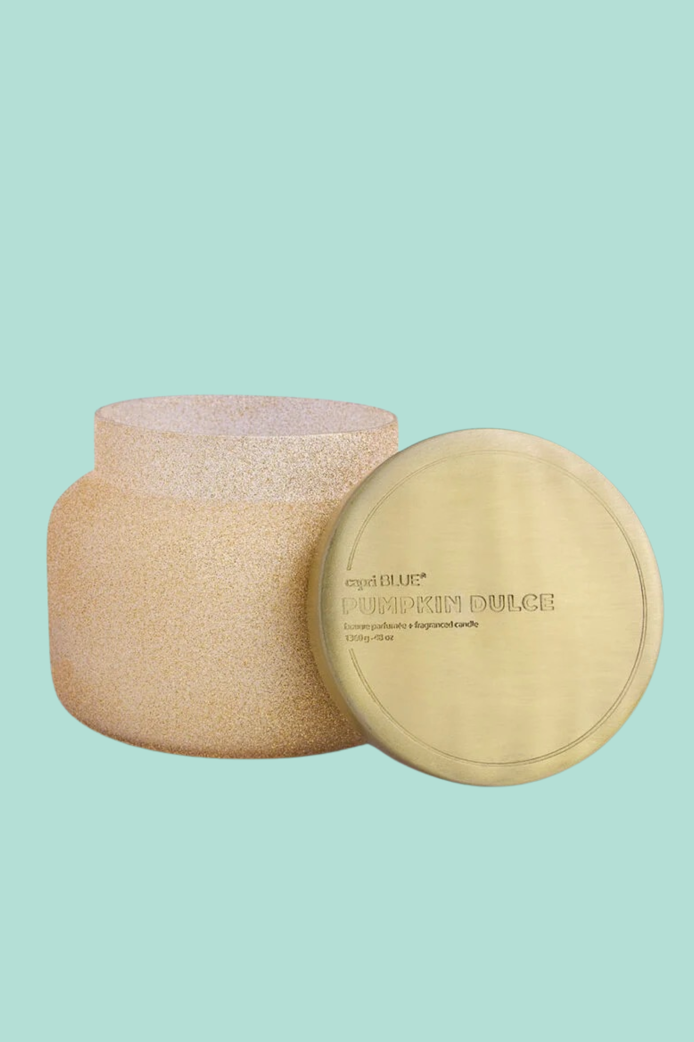 A beige Capri Blue candle jar with a gold lid, adorned with sparkling champagne glitter, showcasing the Pumpkin Dulce Glam fragrance.