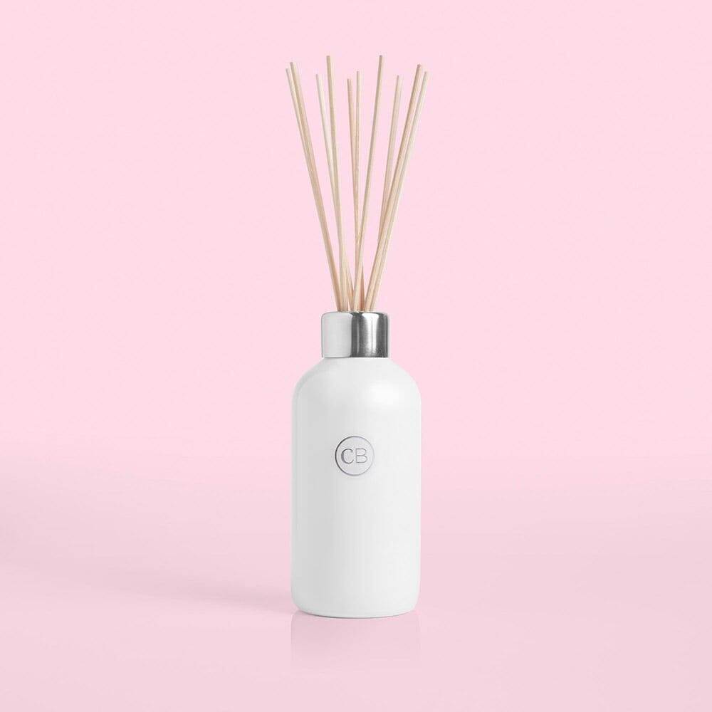 White diffuser bottle with wooden sticks on a pink background