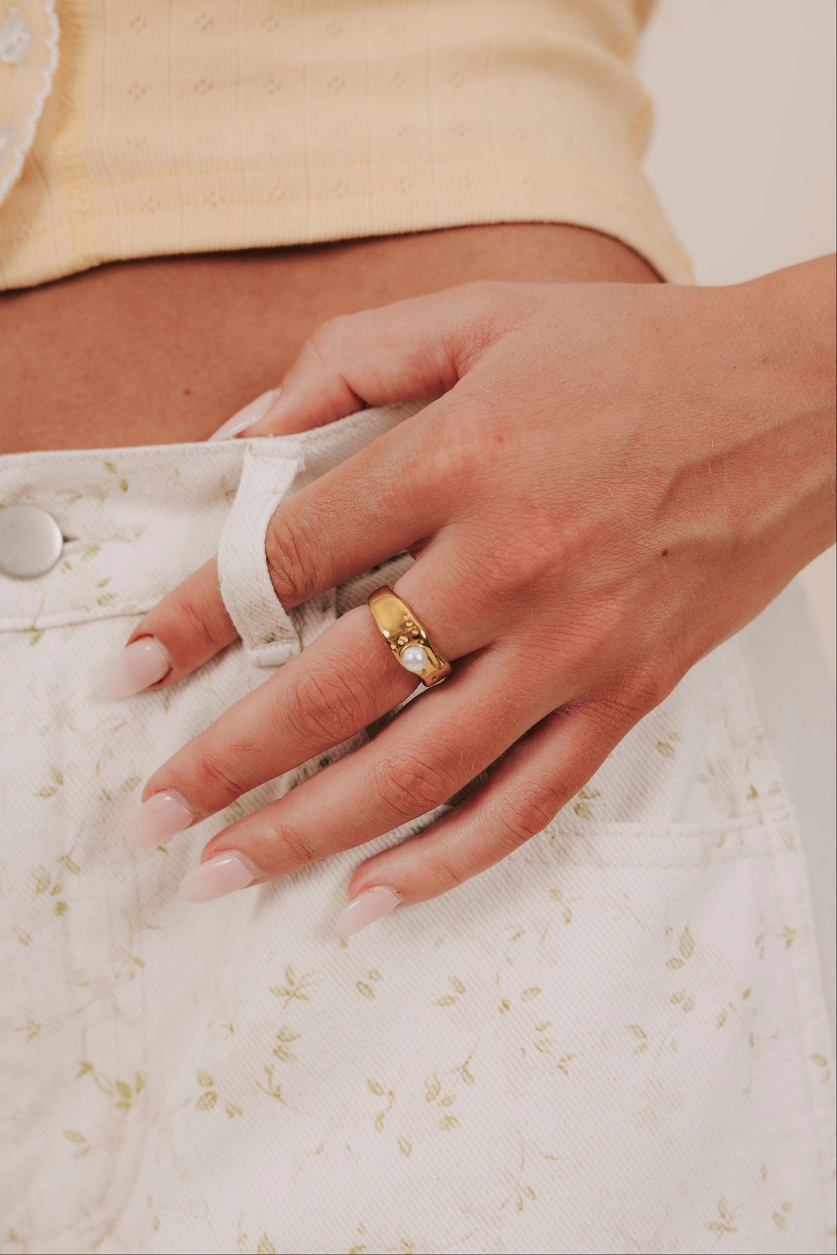 Hand wearing a gold ring on a light background
