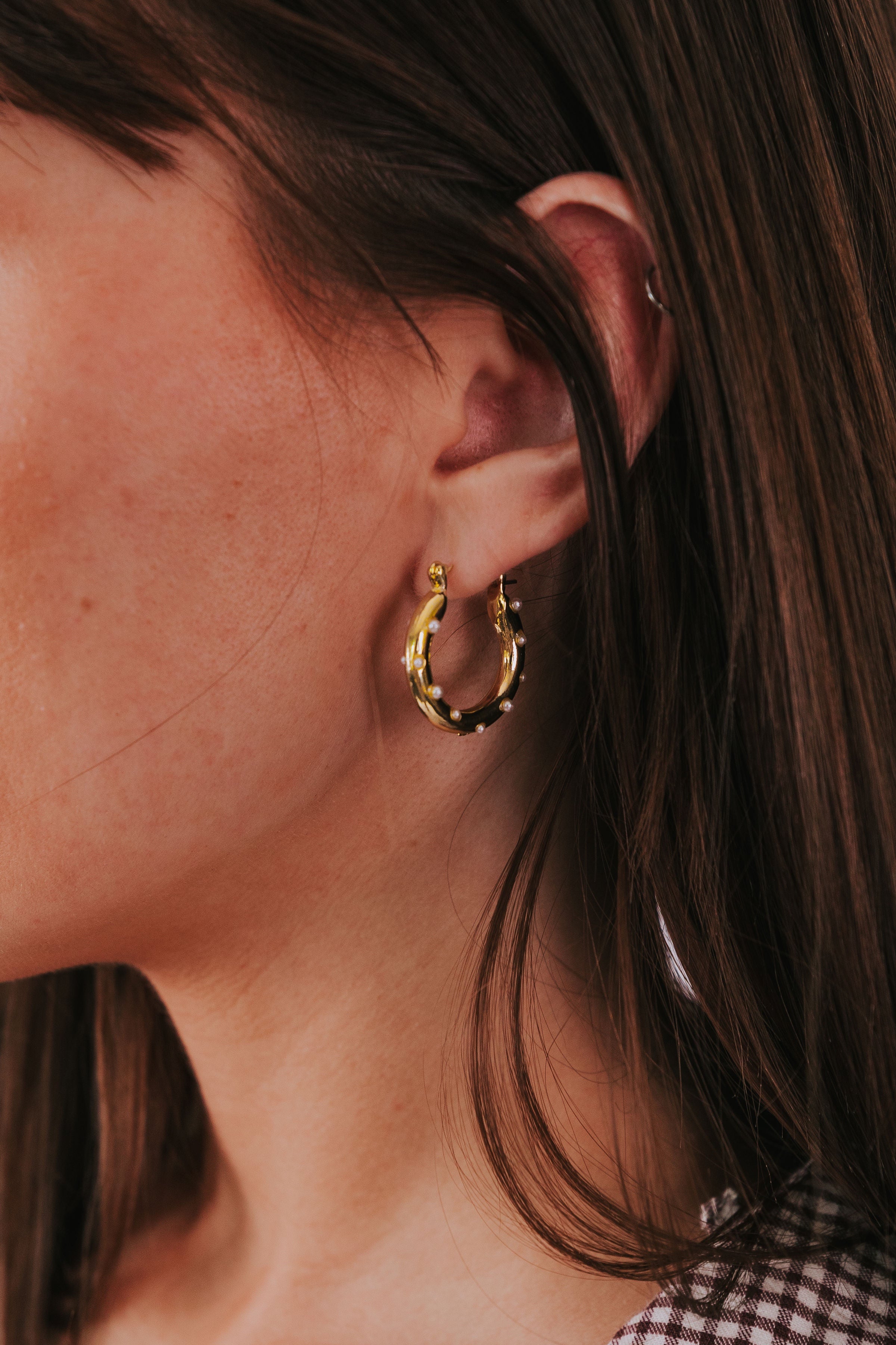 Close-up of a person wearing gold hoop earrings with a blurred background