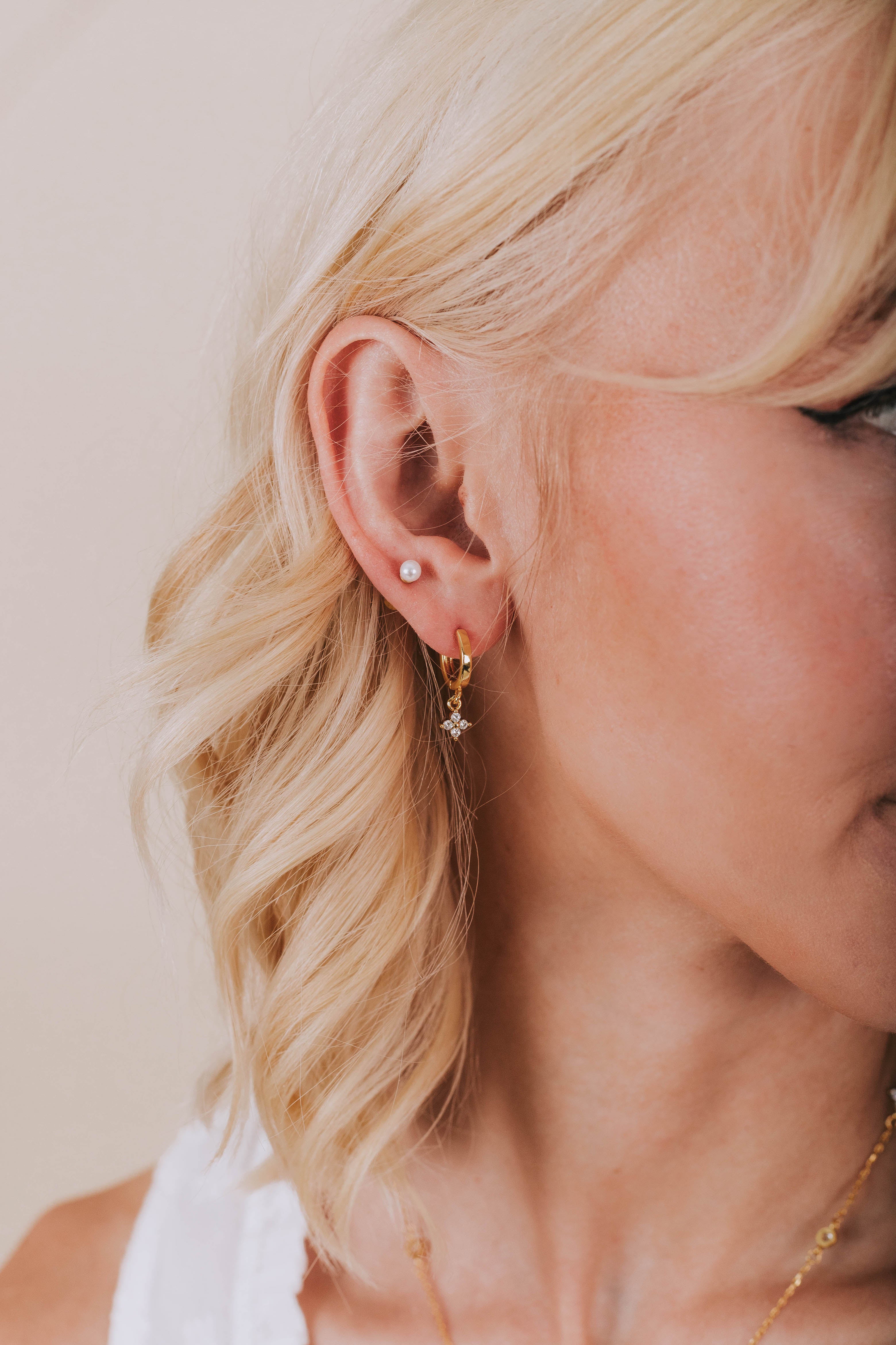 Model wearing gold plated hoop earring with rhinestone flower clover dangle