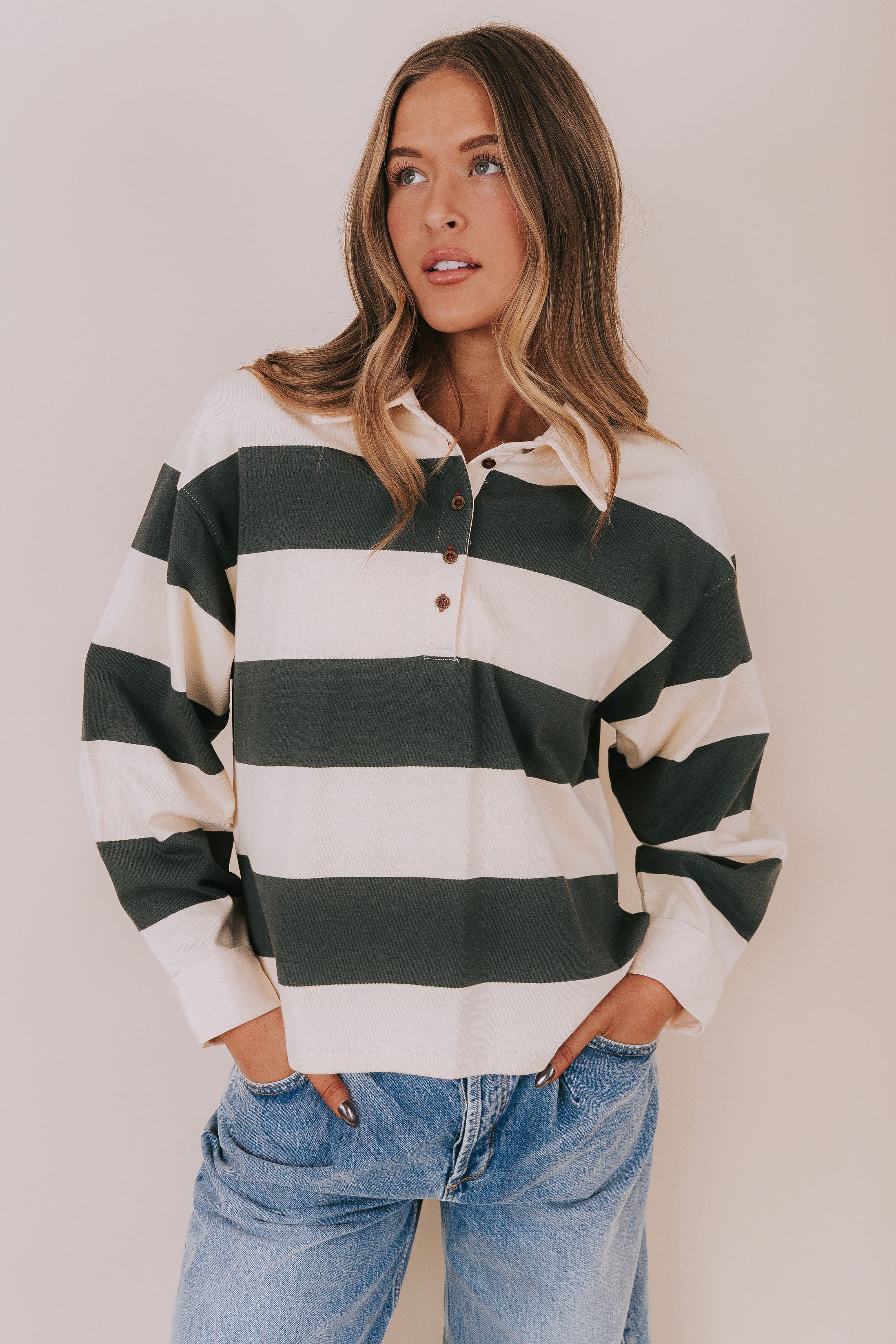Woman wearing a green and white striped shirt with blue jeans against a plain background