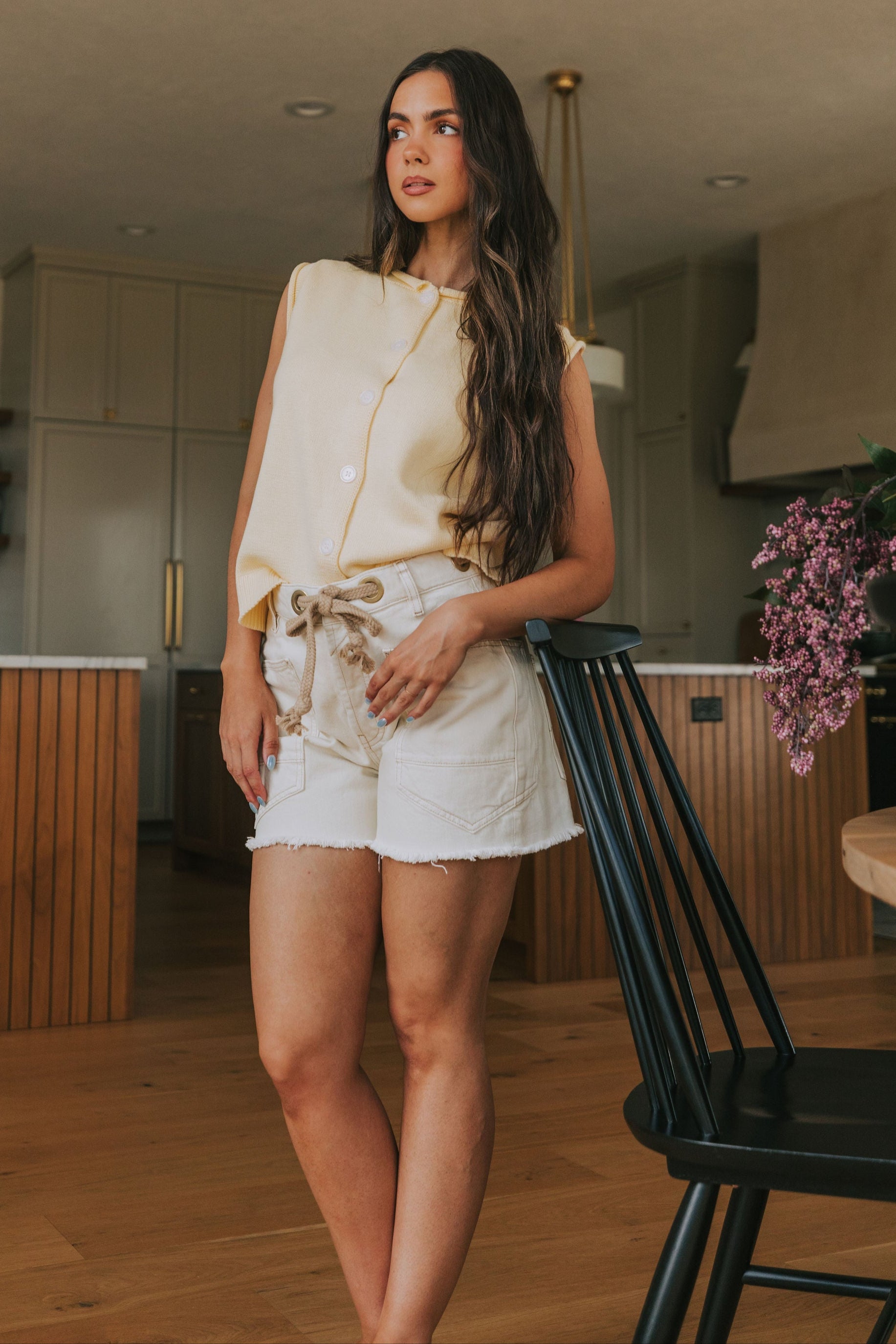 Woman standing in a kitchen wearing a yellow top and white shorts.