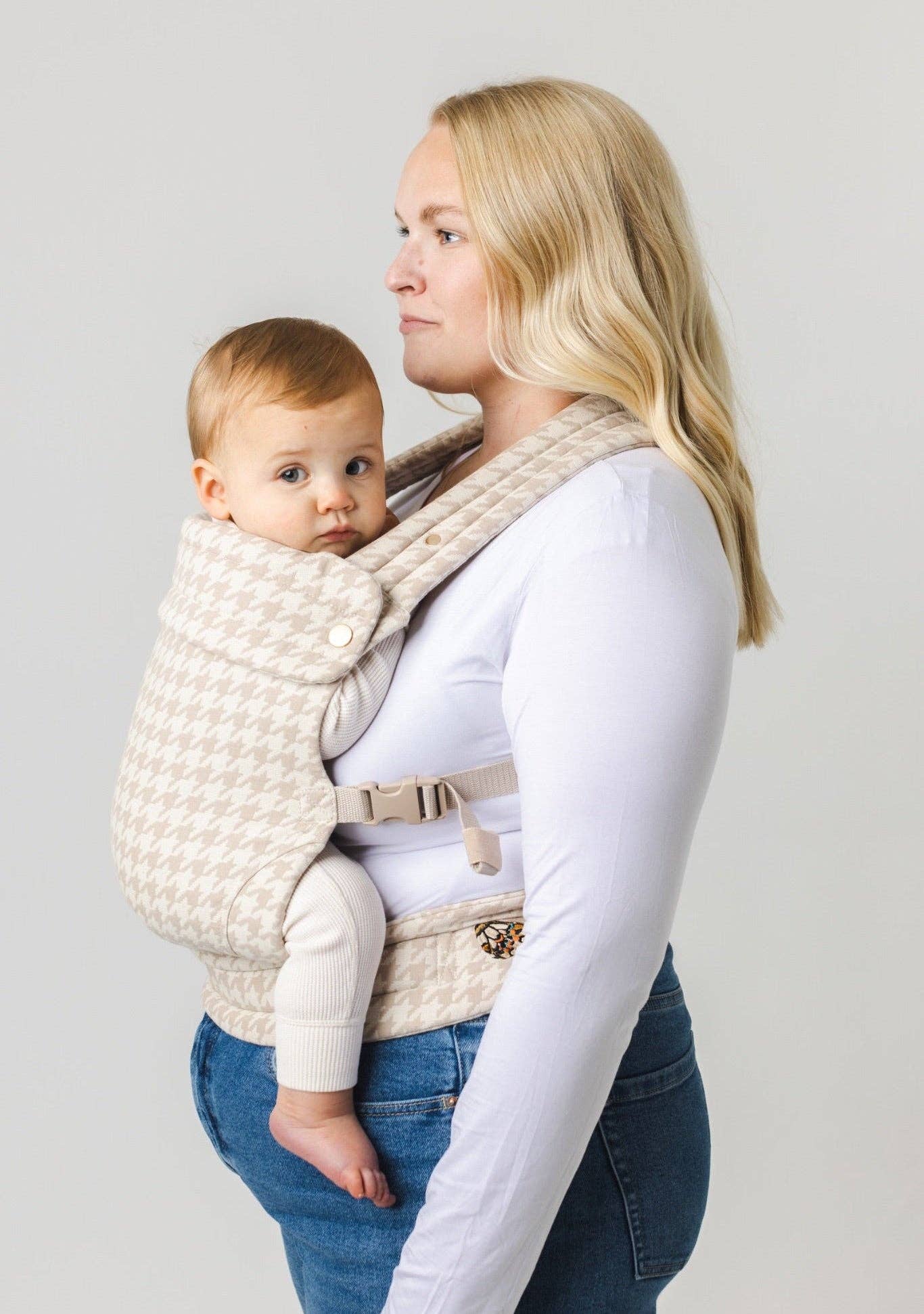 Woman carrying a baby in a textured baby carrier against a plain background