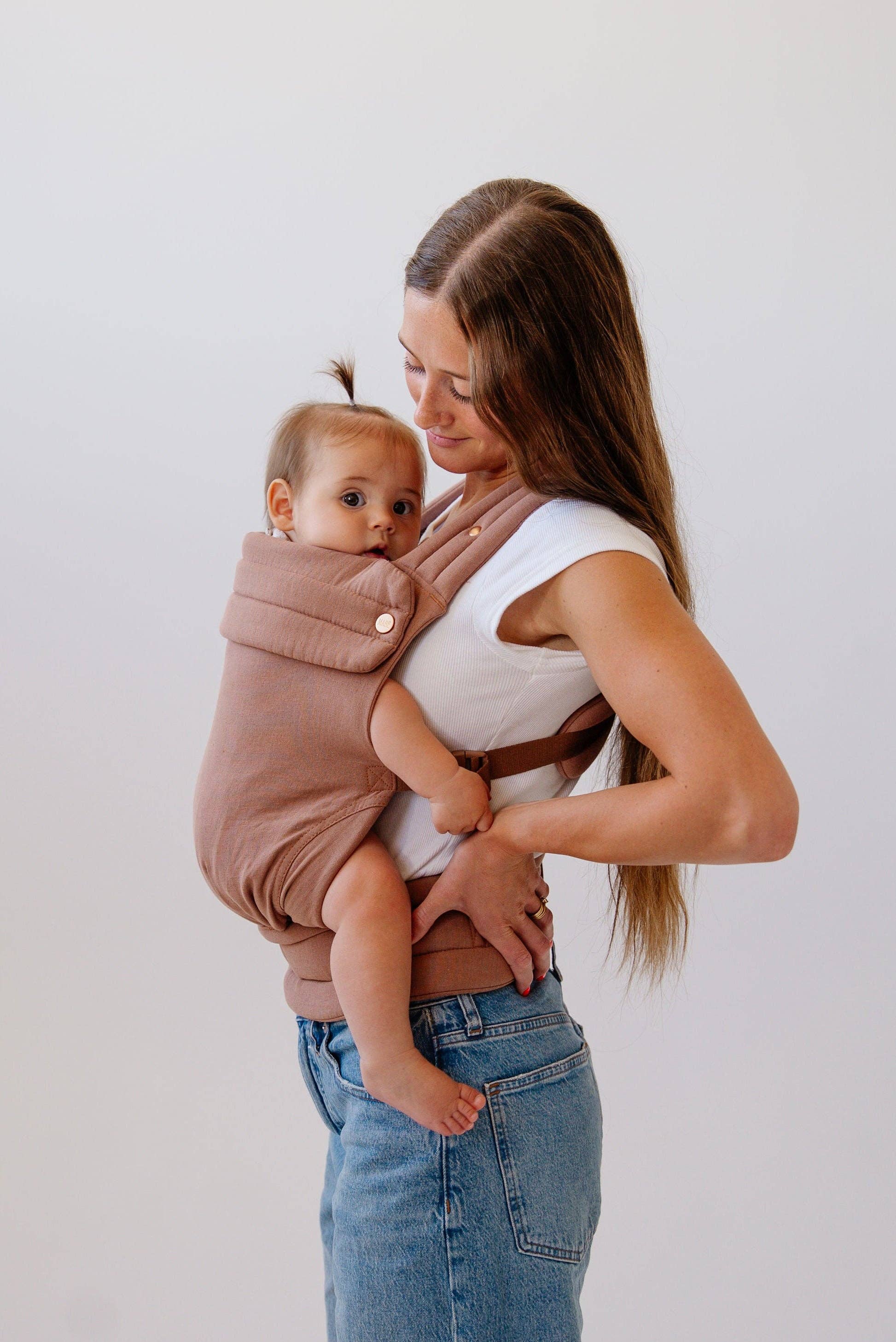 Woman holding a baby in a brown baby carrier against a white background