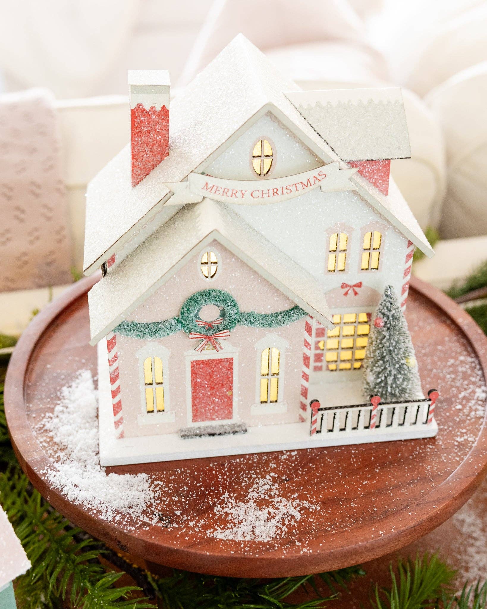Decorative Christmas house with tree, wreath, and glitter snow accents, with a banner reading 'Merry Christmas'.