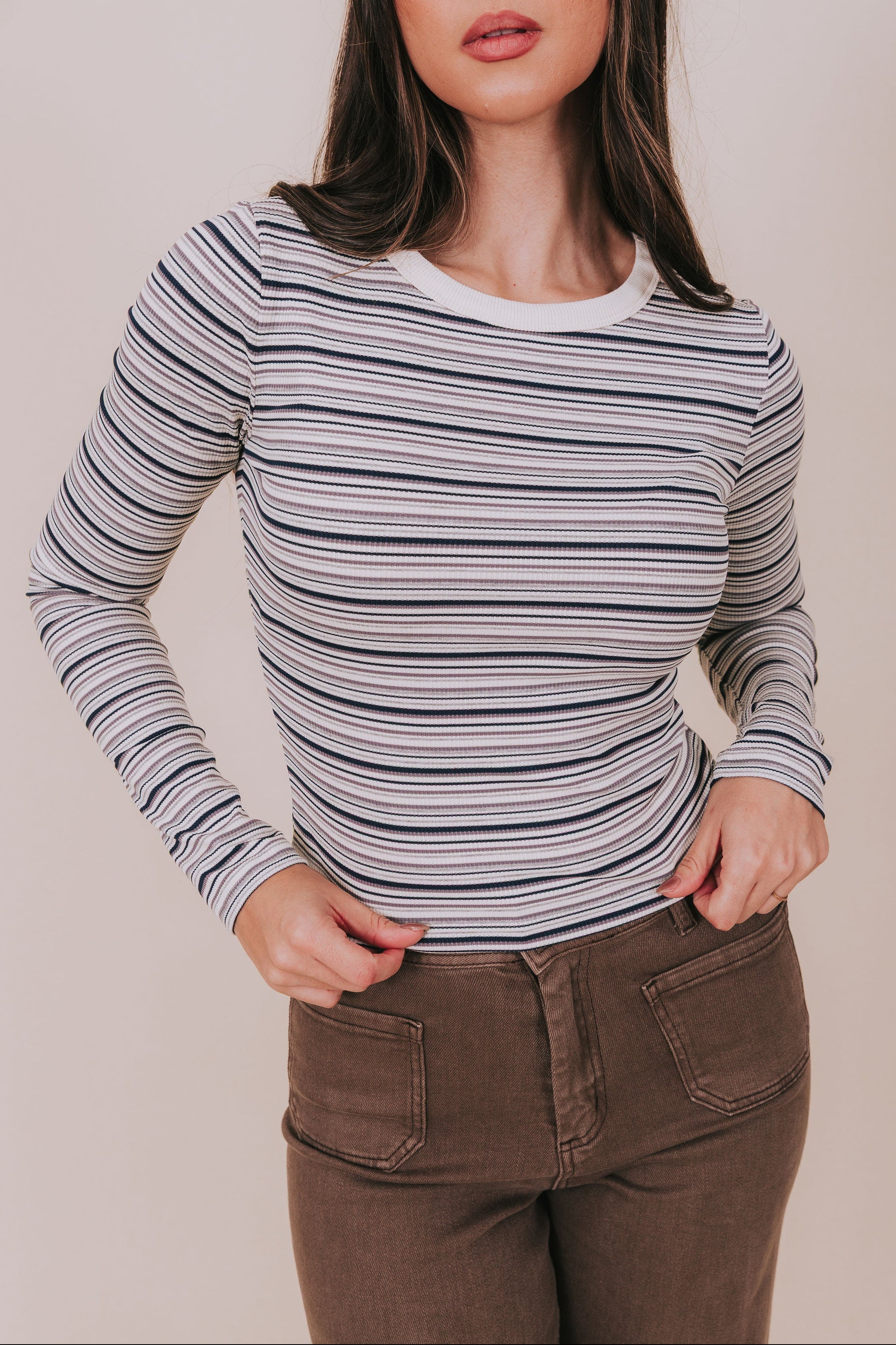 Woman wearing a striped long-sleeve top and brown pants against a plain background