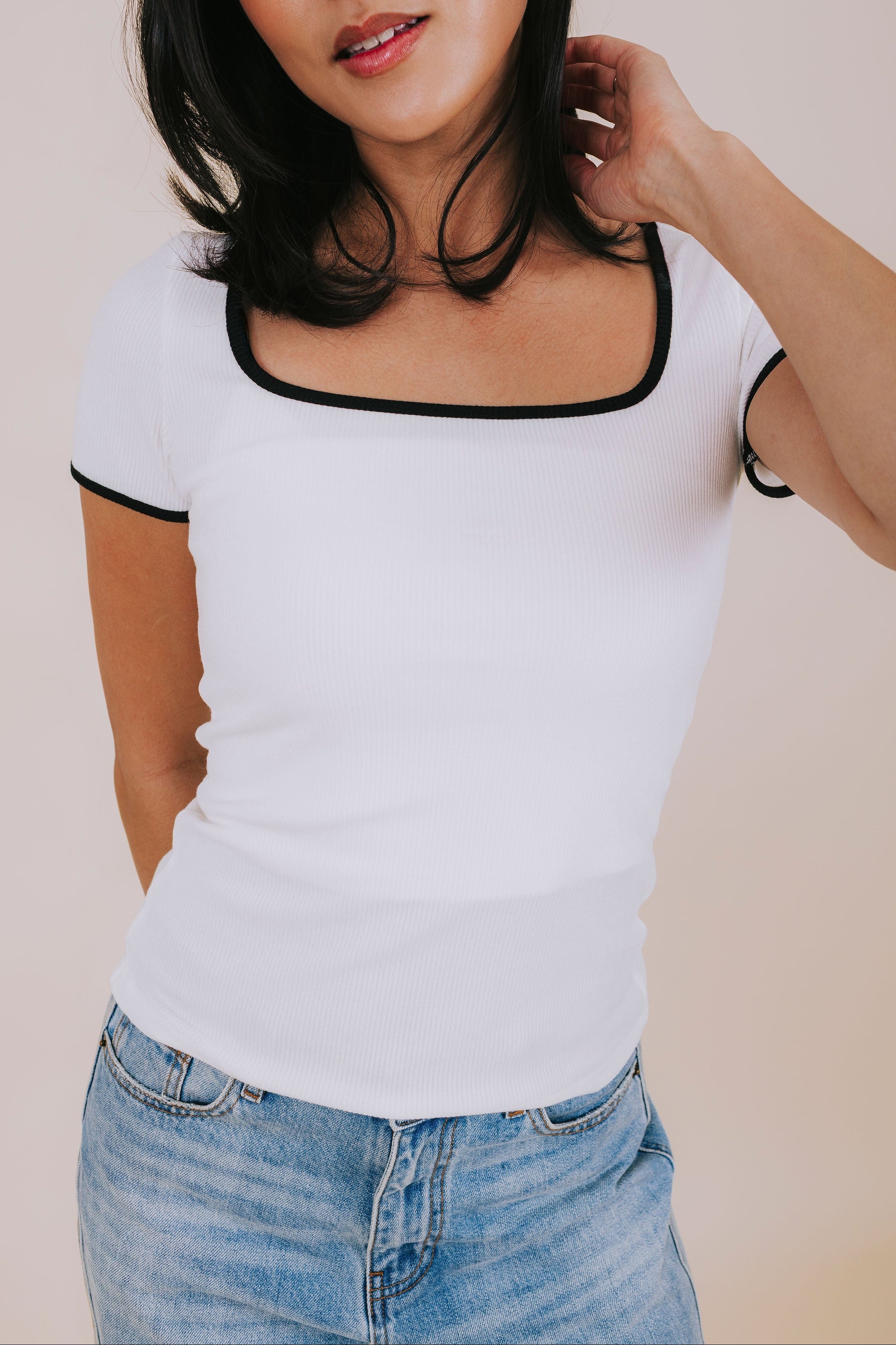 Woman wearing a white top with black trim and blue jeans against a plain background
