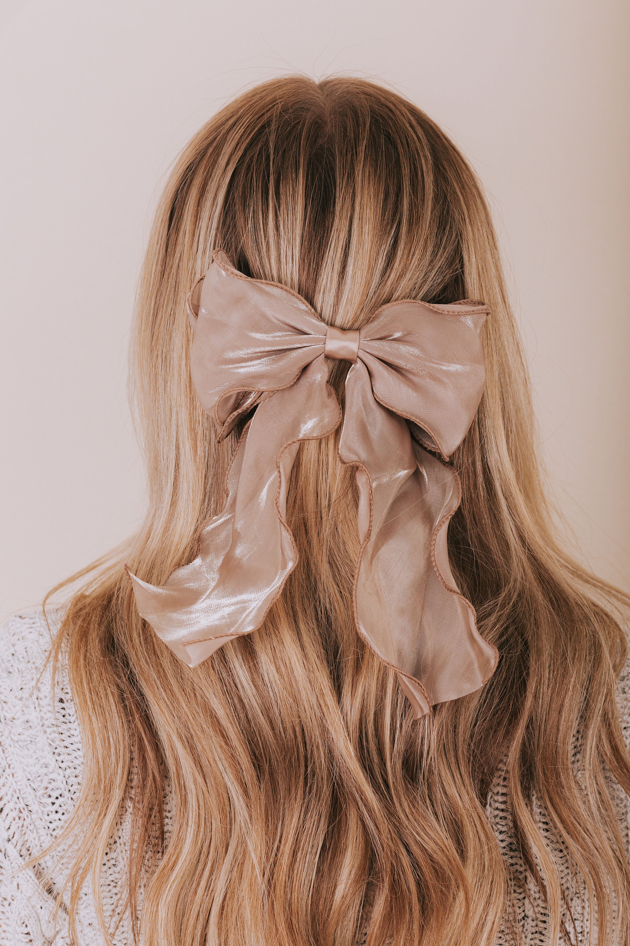 Long blonde hair with a large beige bow against a neutral background