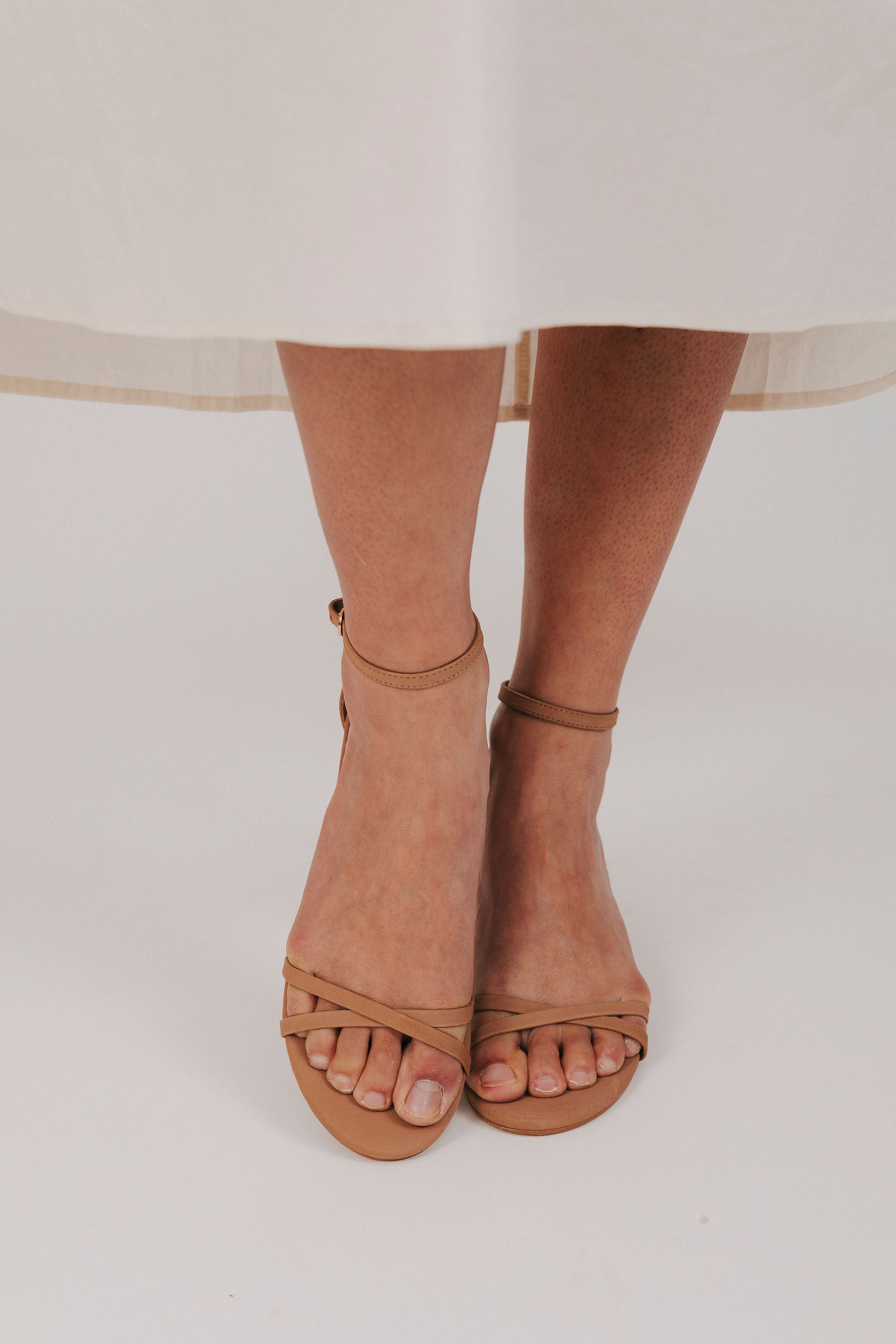 Brown open-toe sandals worn with a light-colored skirt on a white background