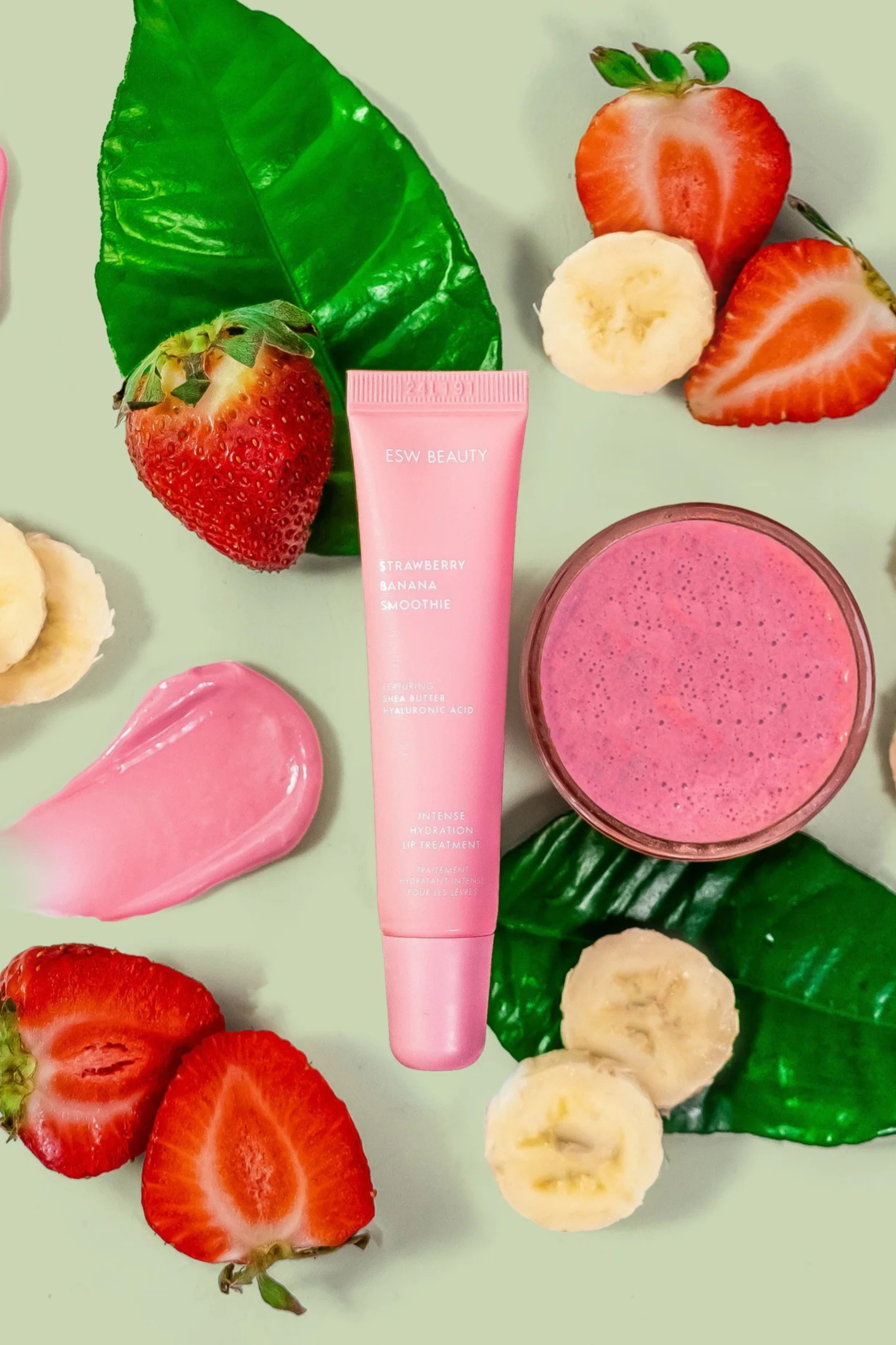 Pink lip care and gloss product with strawberries, bananas, and a smoothie on a light green background
