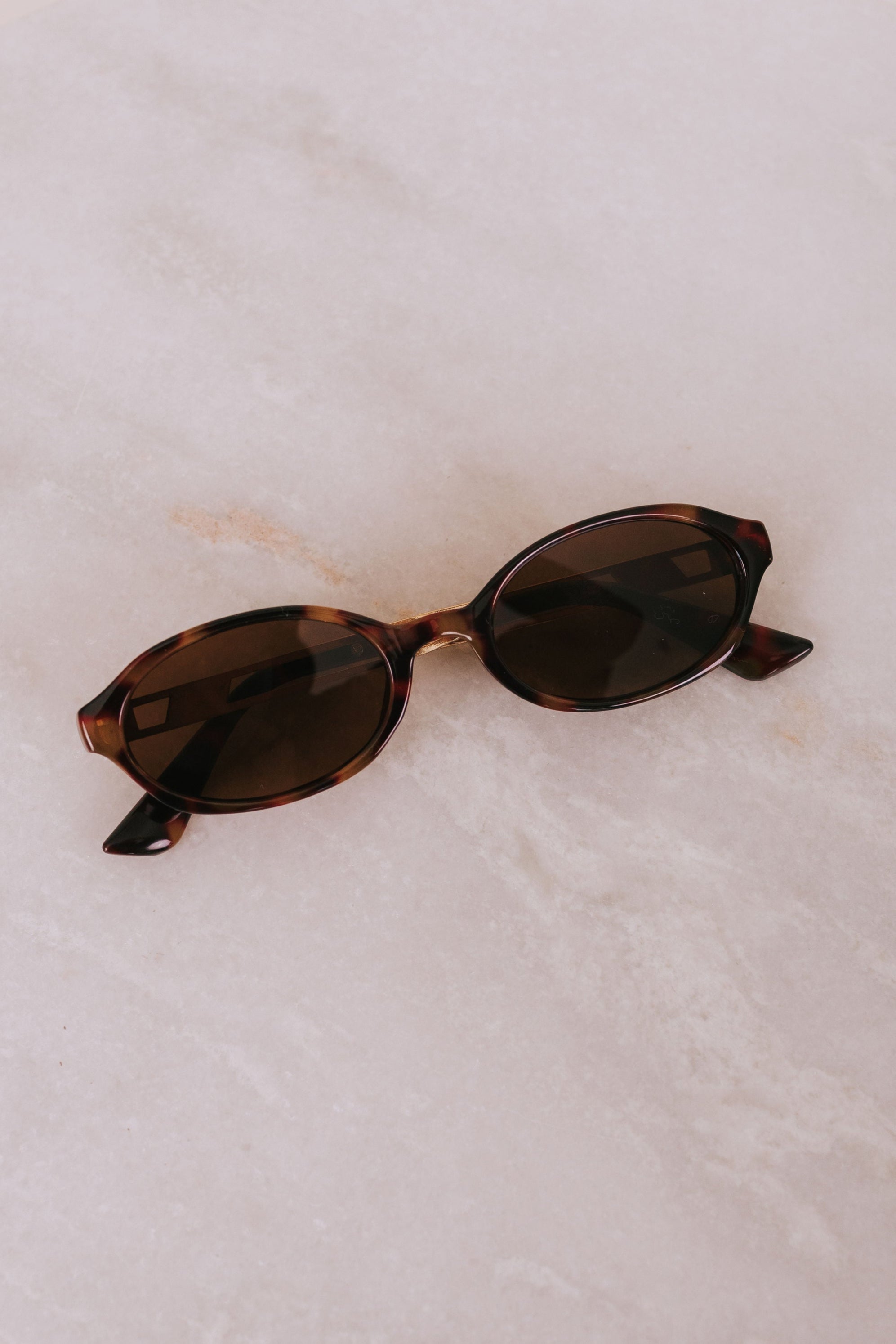 Sunglasses with tortoiseshell frame and brown lenses on a light marble background