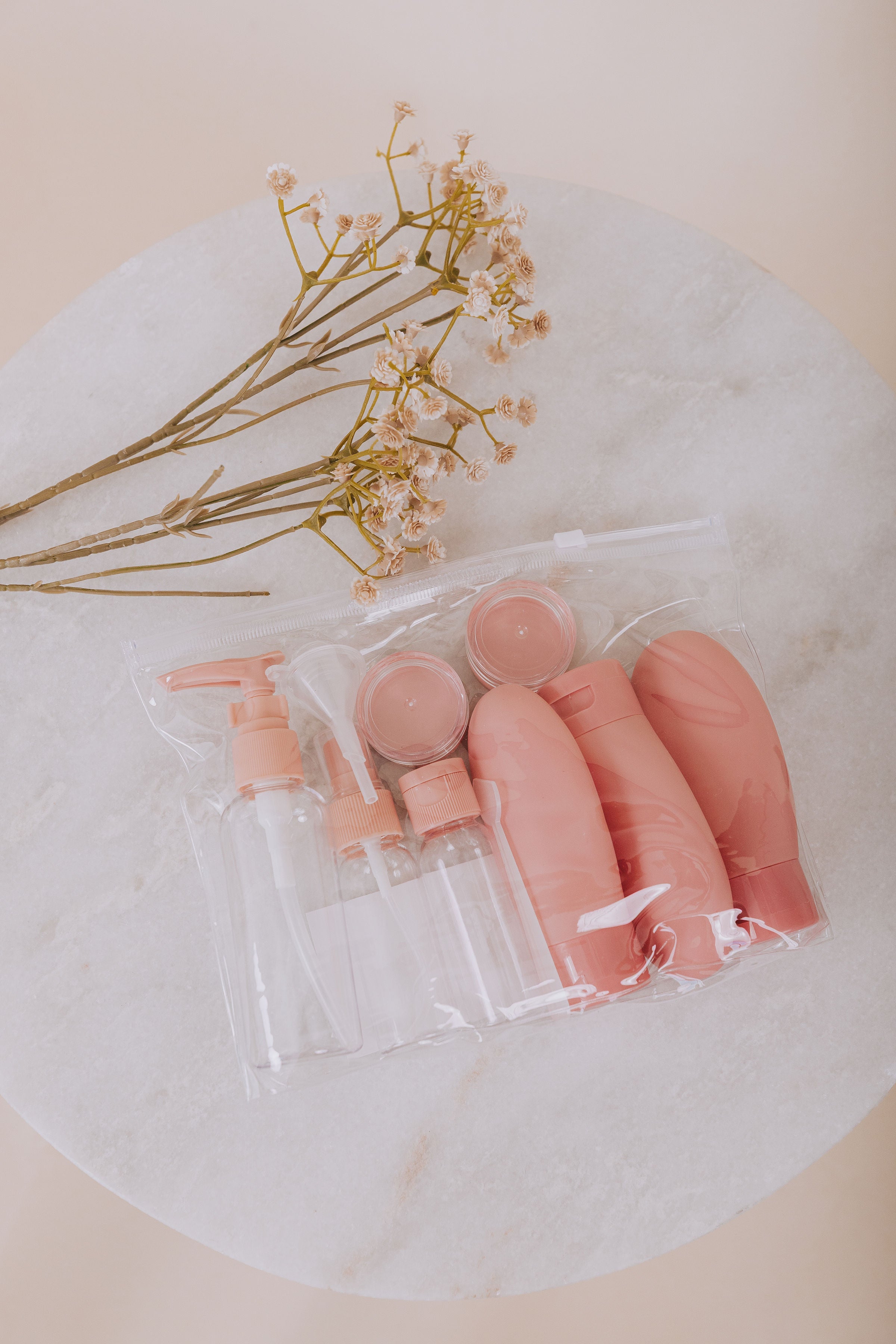 Set of pink travel containers including squeeze bottles, spray bottles, pump bottles, jars, a funnel, and a scoop all in one clear carry bag.