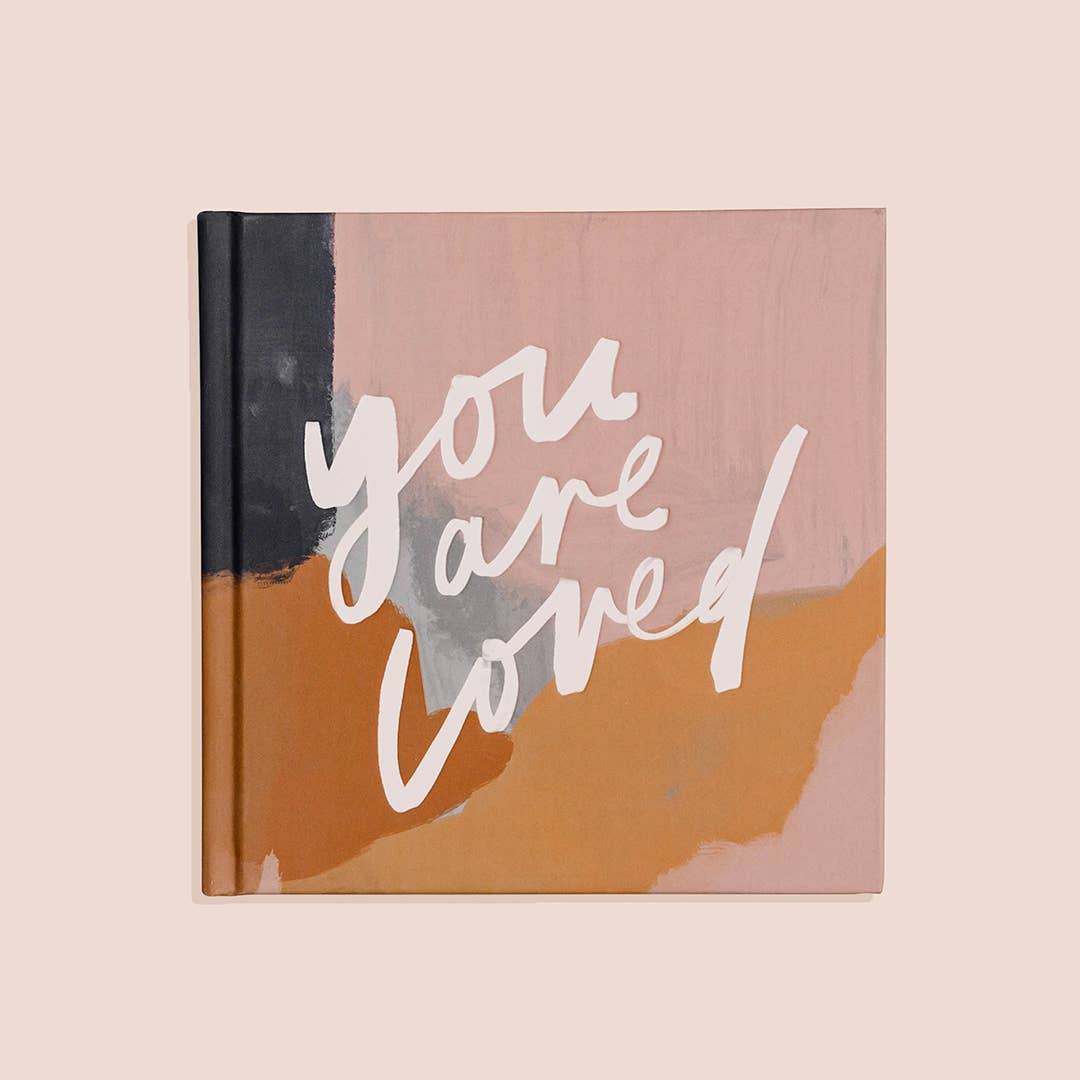 A hardcover coffee table book with a pink and orange abstract design on the cover, titled 'you are loved' in white script.