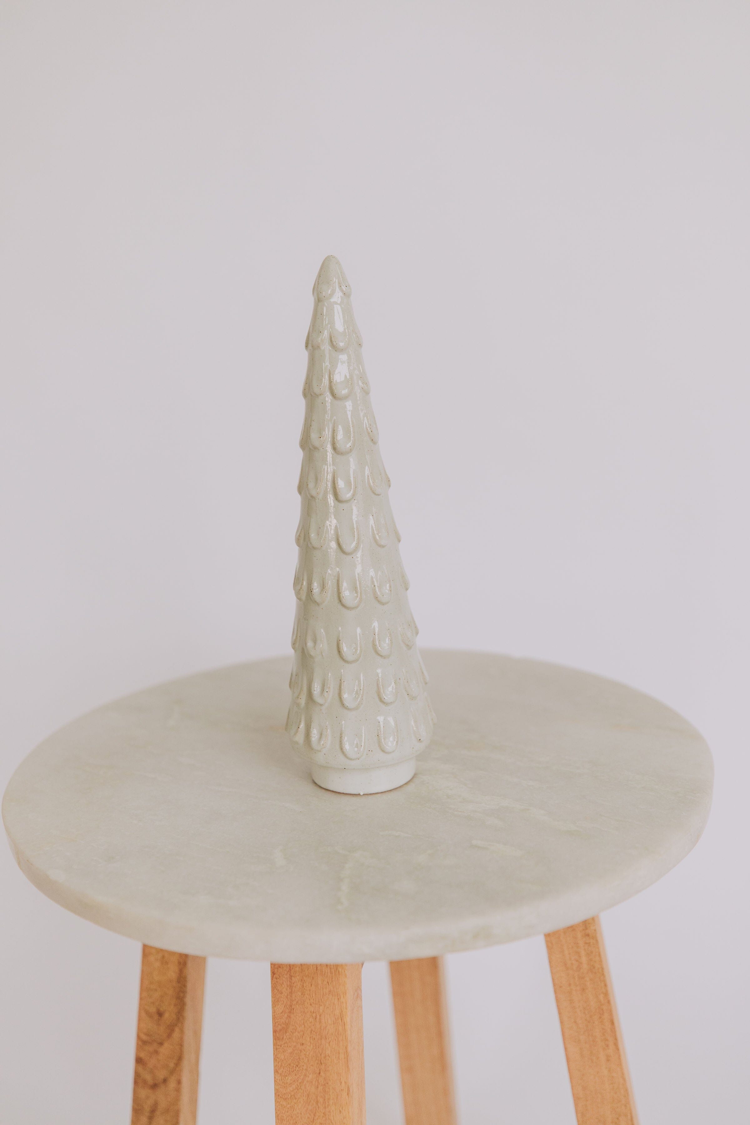 A glazed stoneware tree with a hollow structure, displayed on a round, wooden stool.