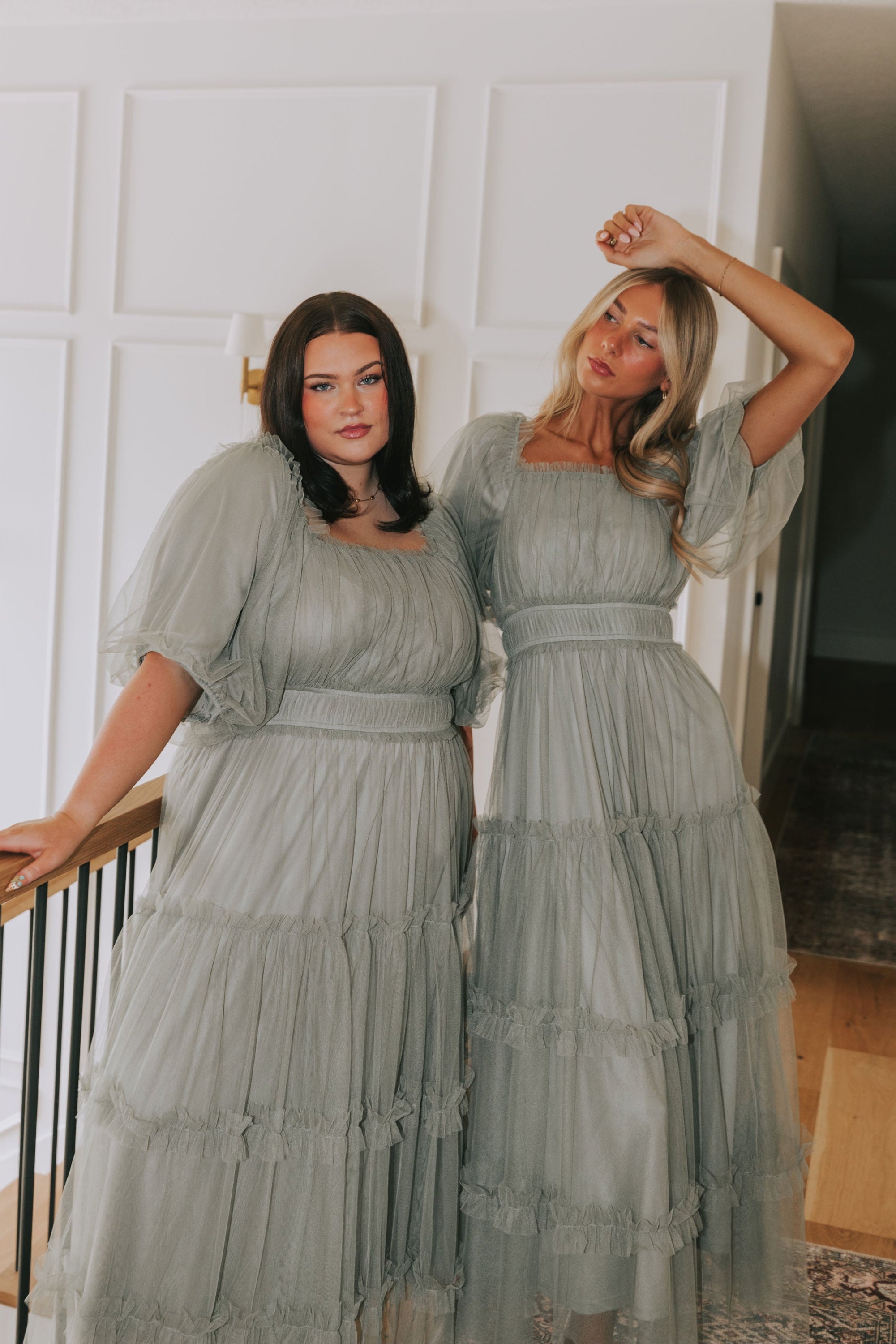 Two women in matching light green dresses standing indoors.