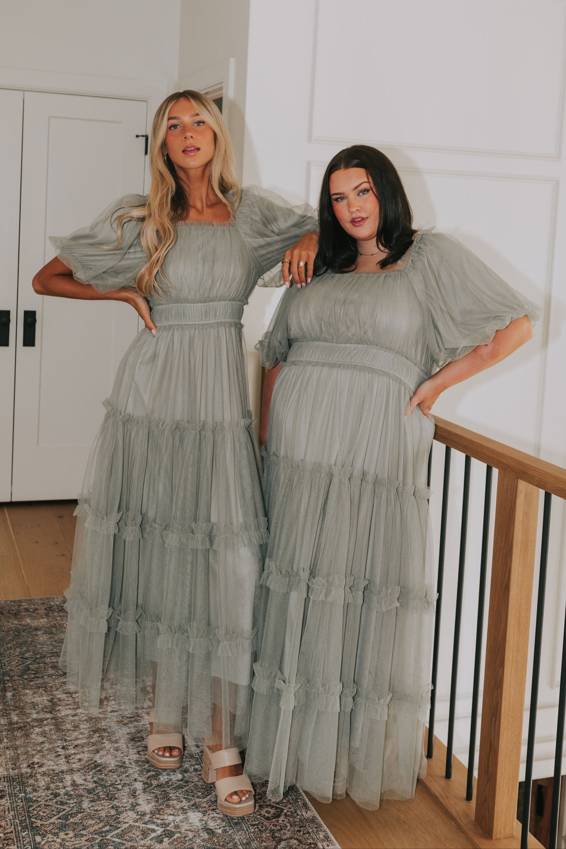 Two women in matching green dresses standing in a home setting.