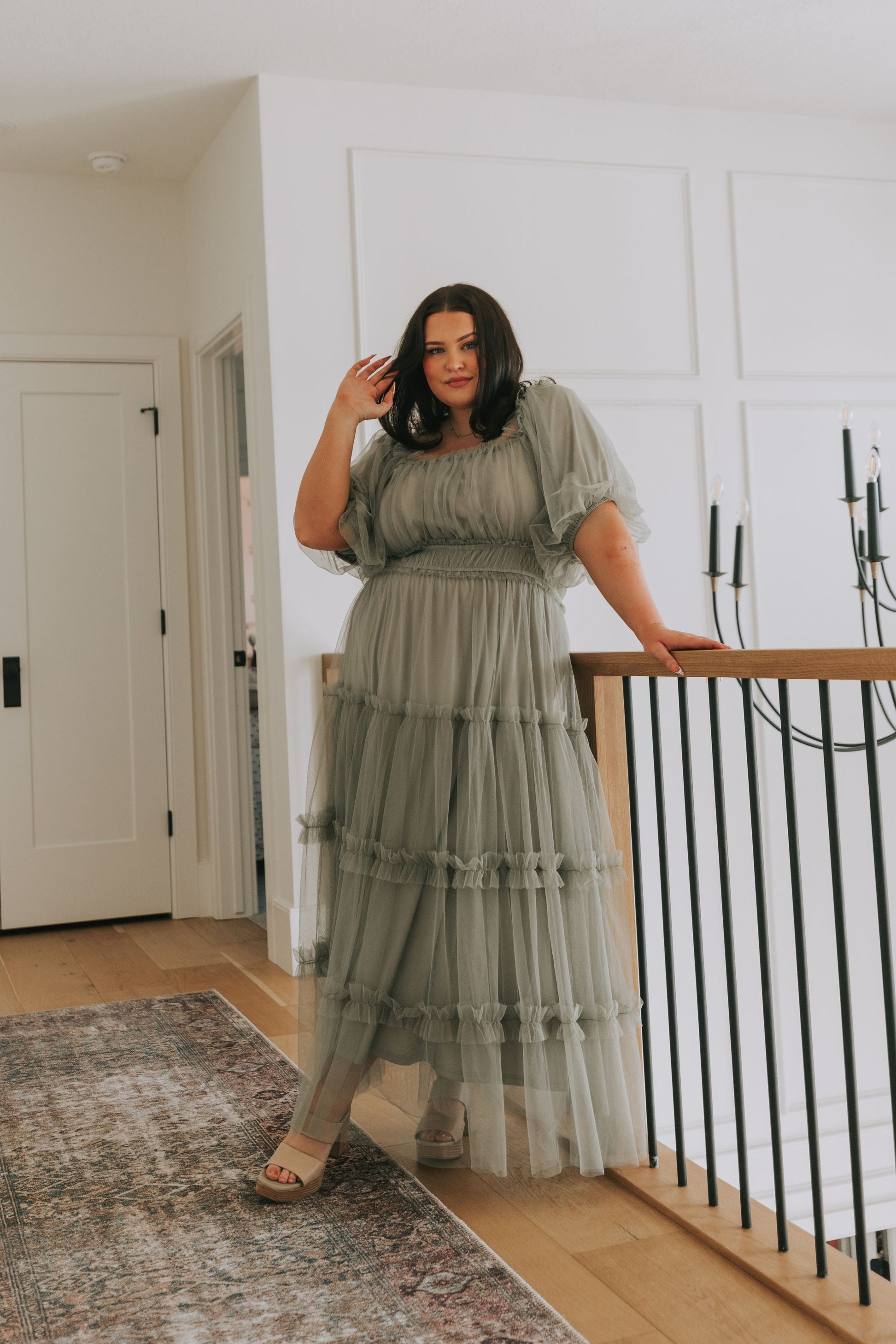 Woman in a green dress standing in a room with white walls and a chandelier.