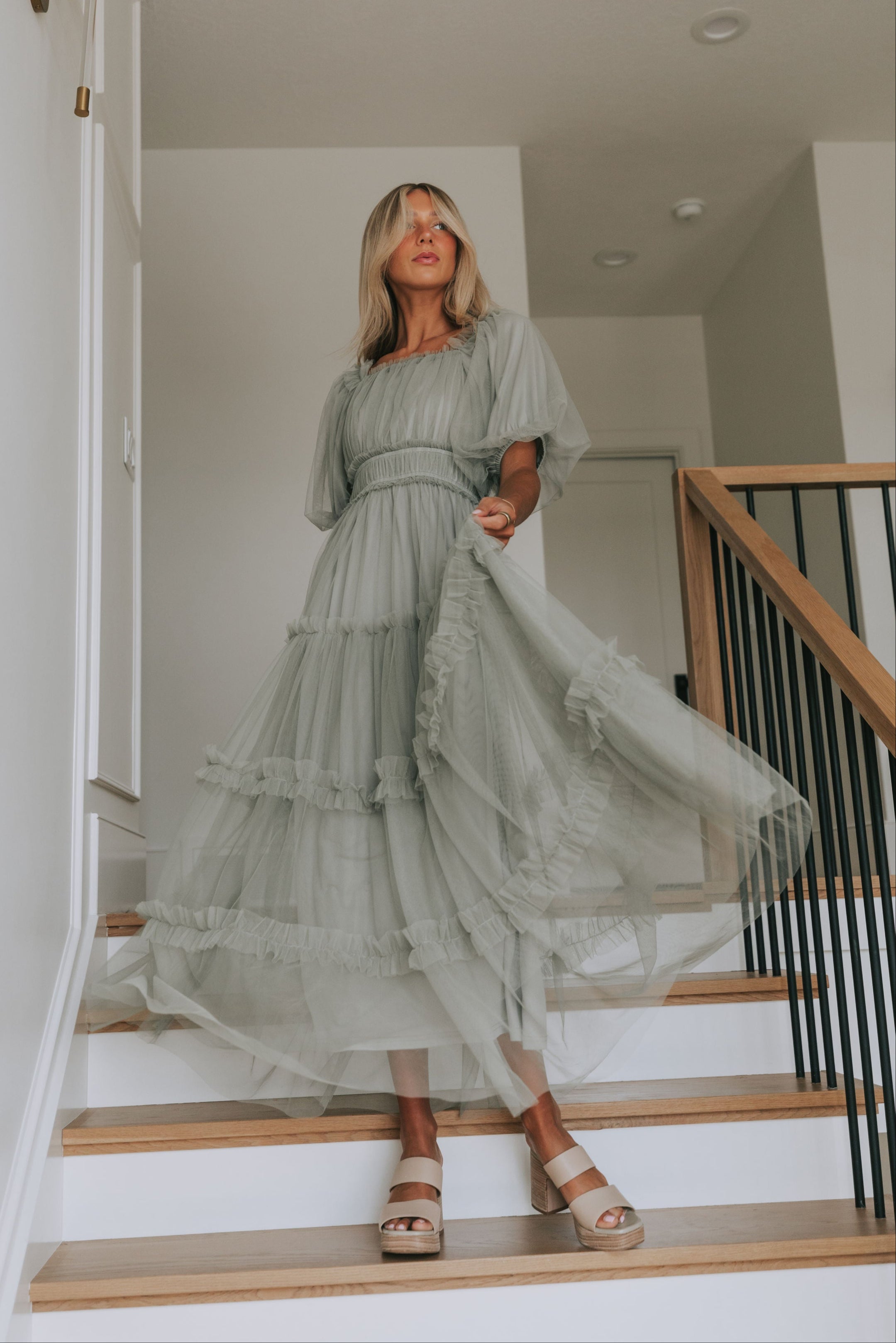 Woman in a flowing dress standing on a staircase in a home setting