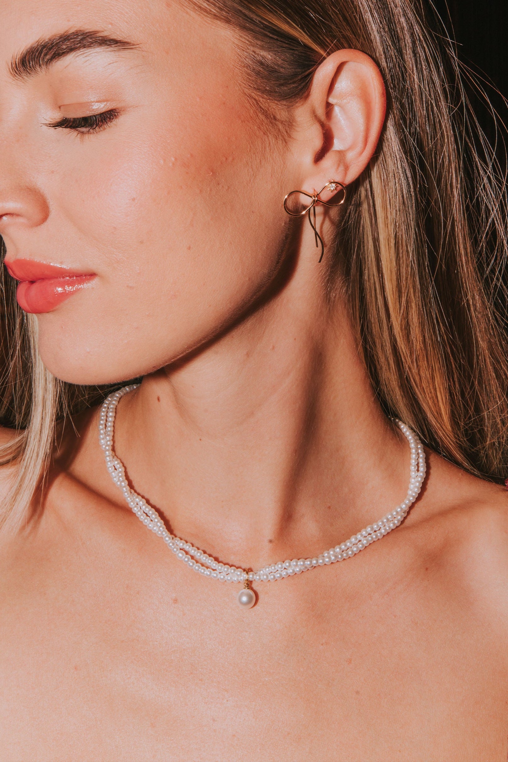 A woman wearing a double layer pearl necklace with gold accents and a pearl pendant.