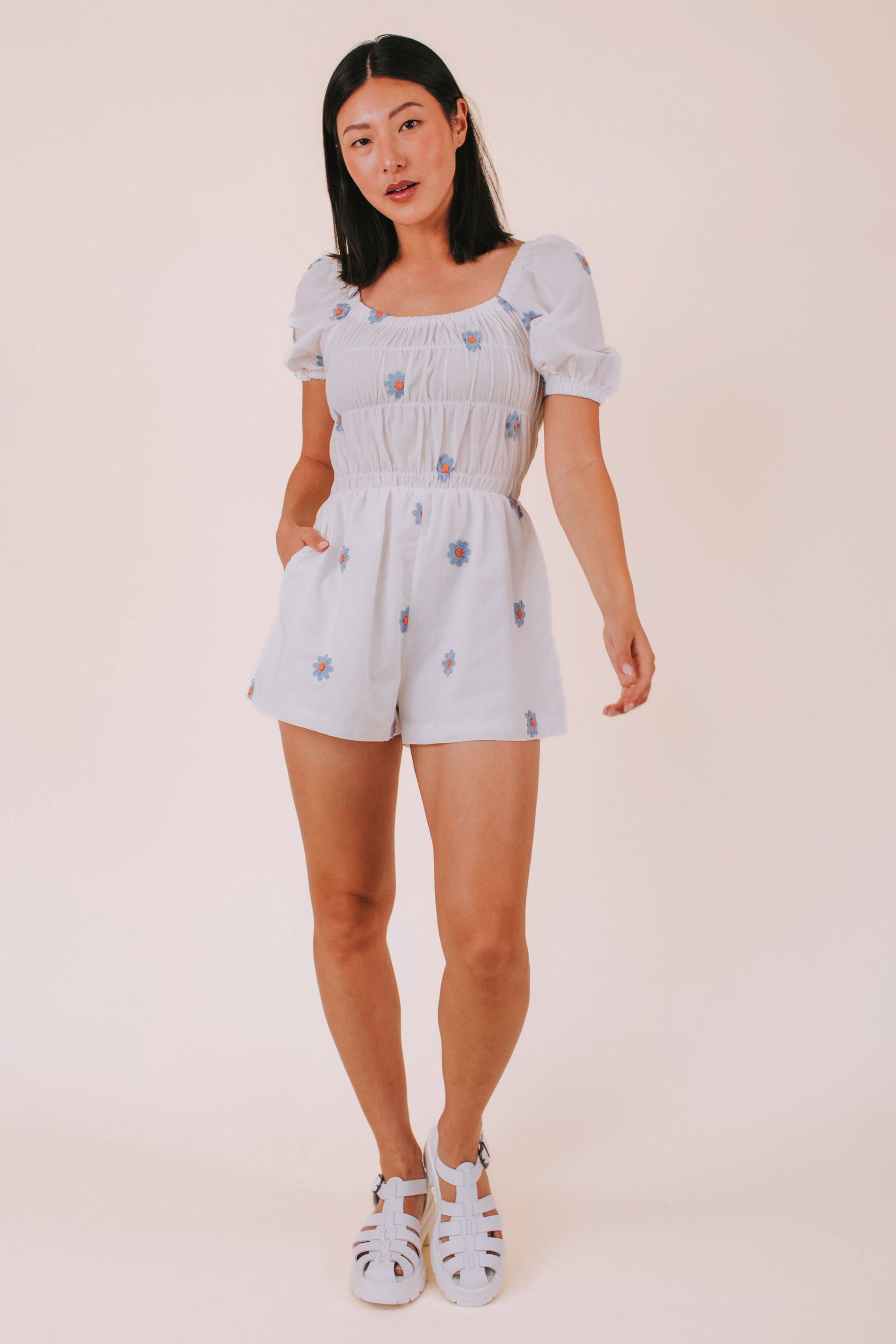 Woman wearing a white romper with blue daisies against a plain background