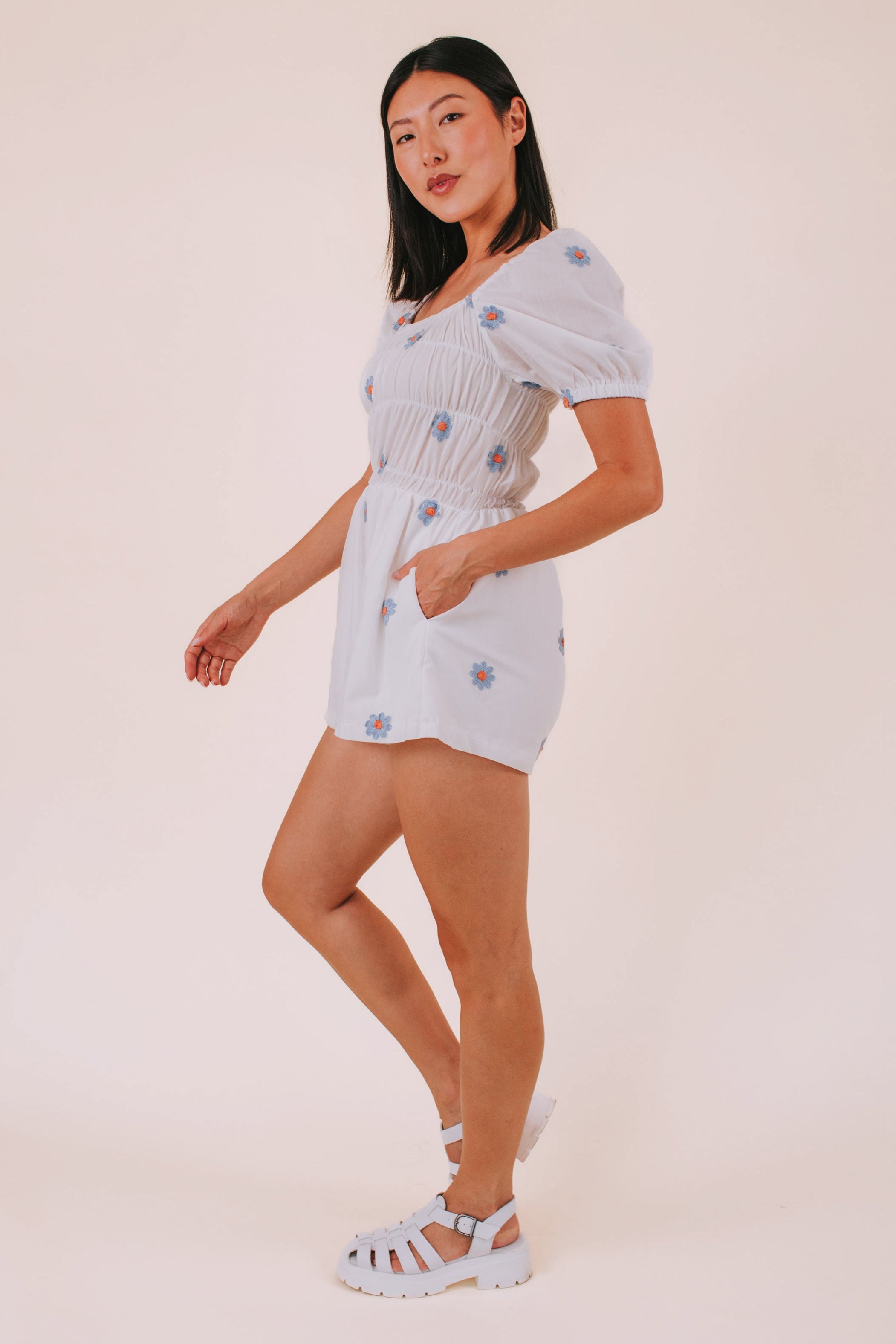 Woman wearing a white romper with blue daisies against a plain background
