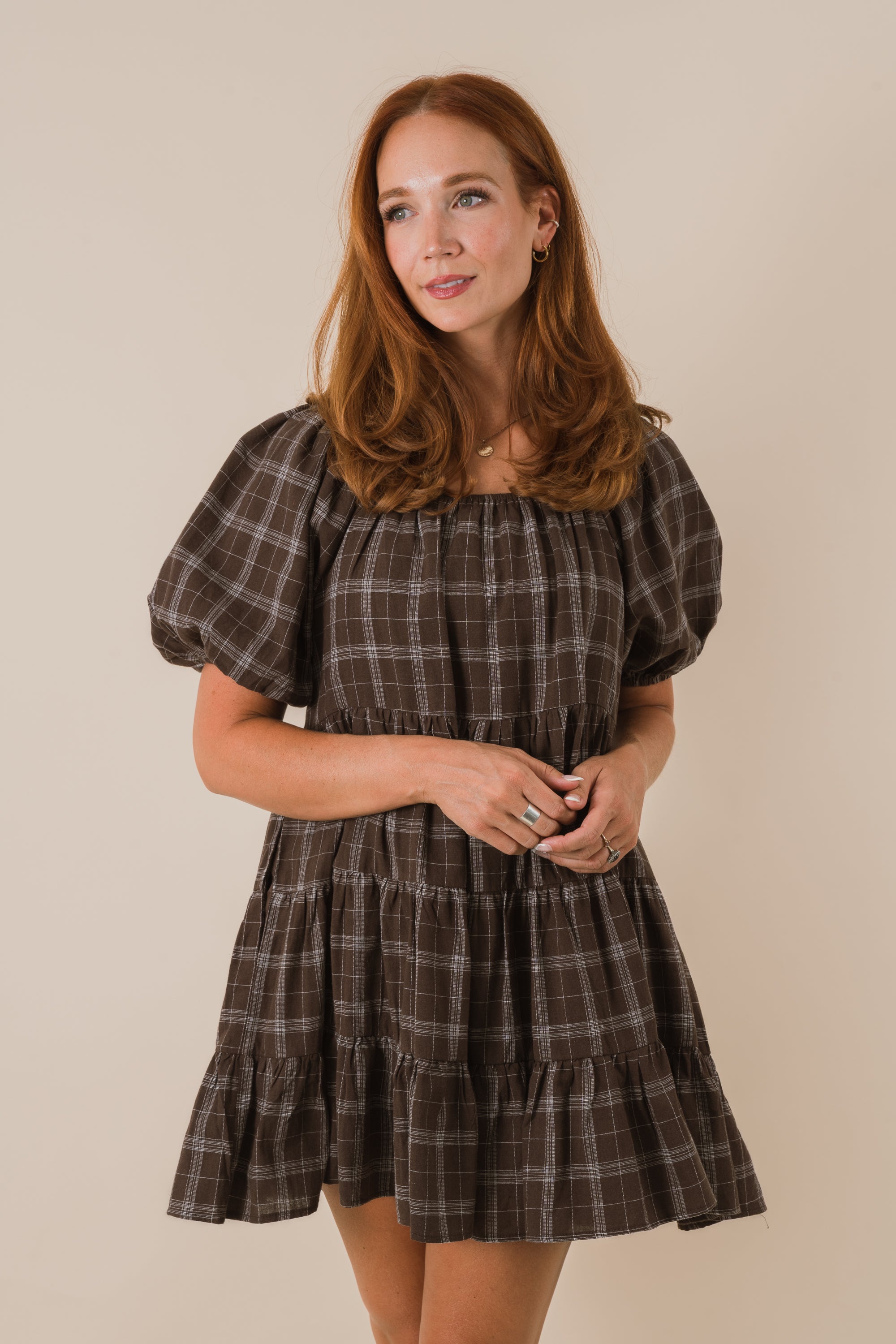 Woman wearing a plaid dress with puff sleeves against a beige background