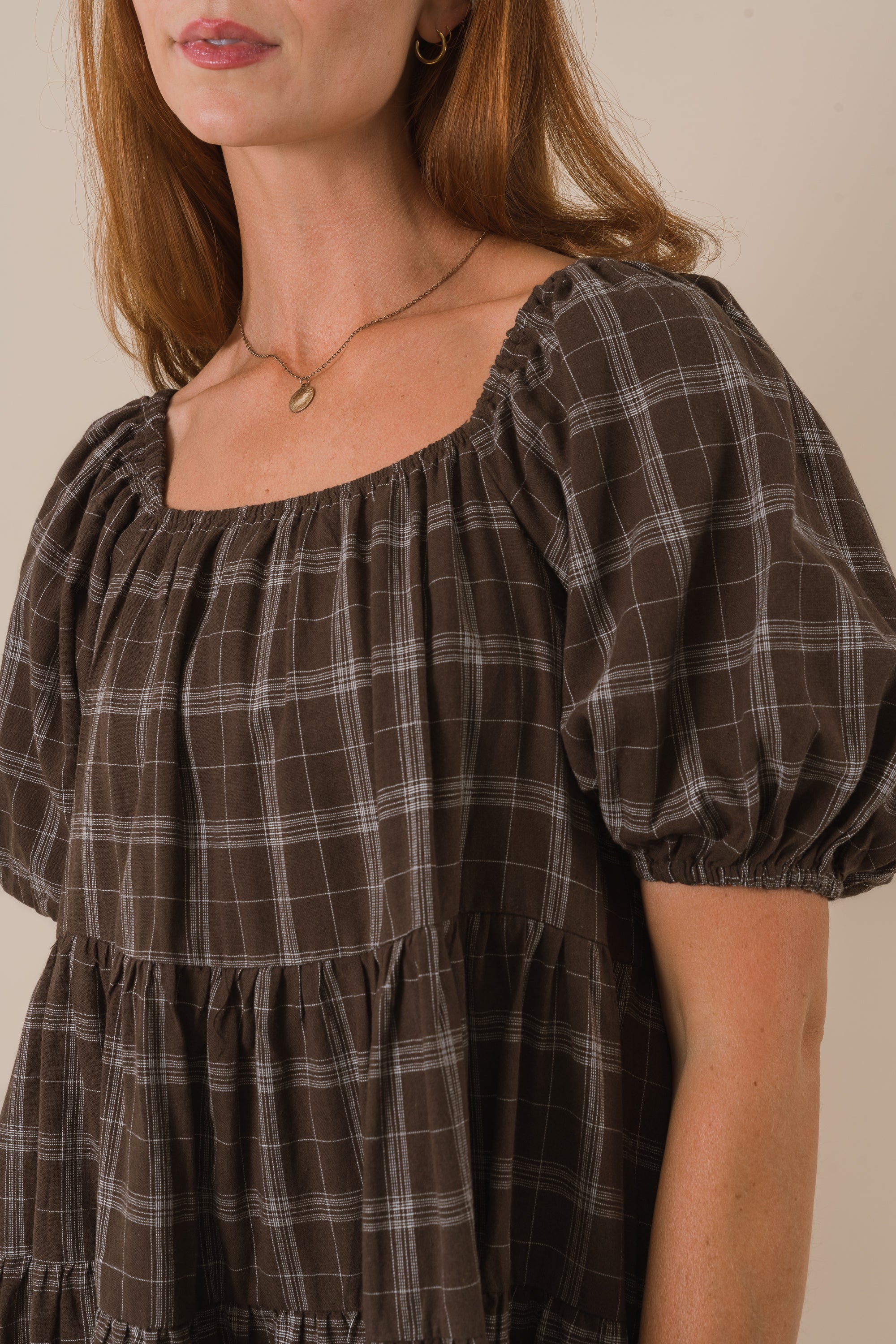 Brown plaid dress with puffed sleeves worn by a person on a neutral background