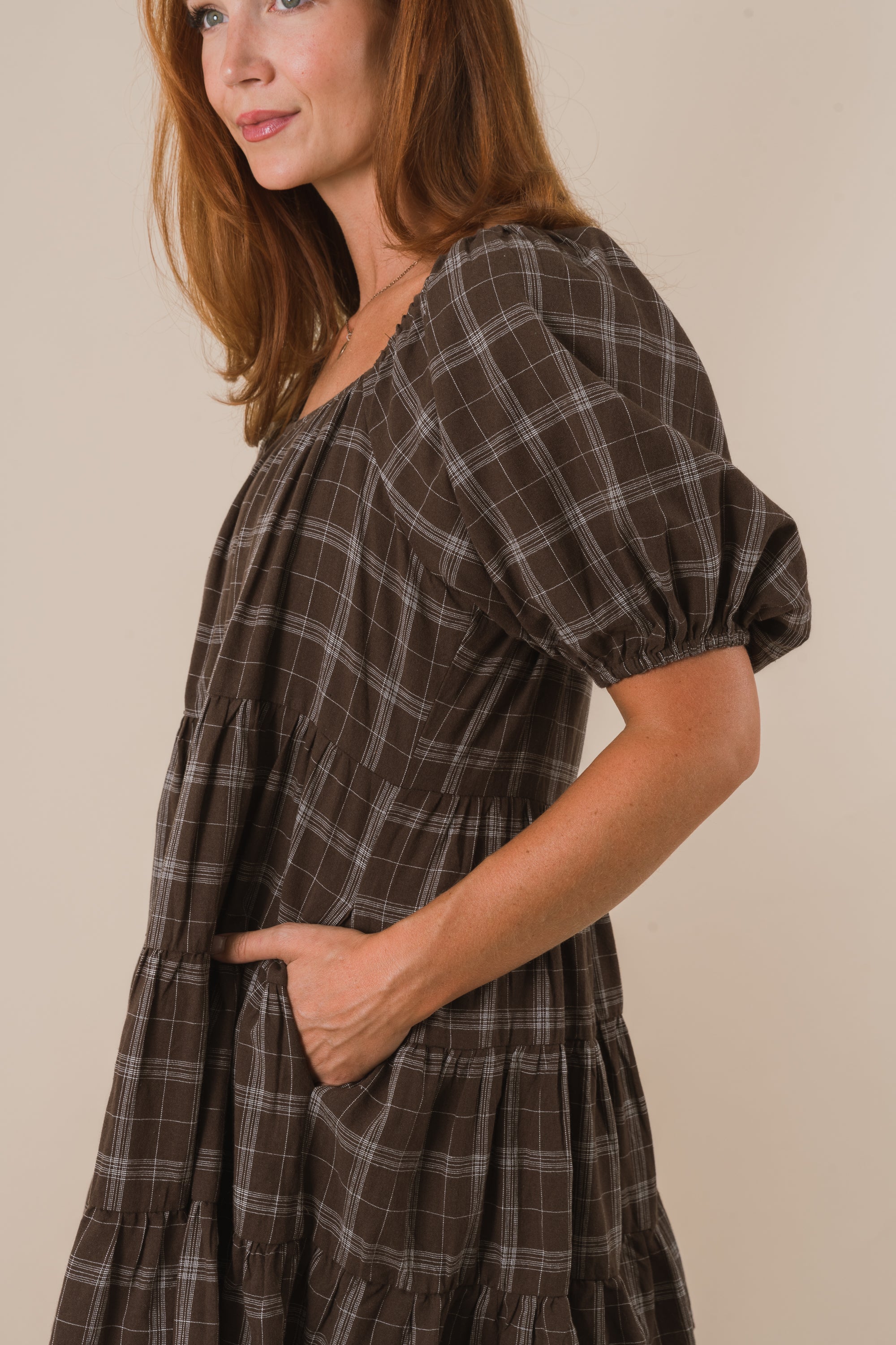 Woman wearing a brown plaid dress against a beige background