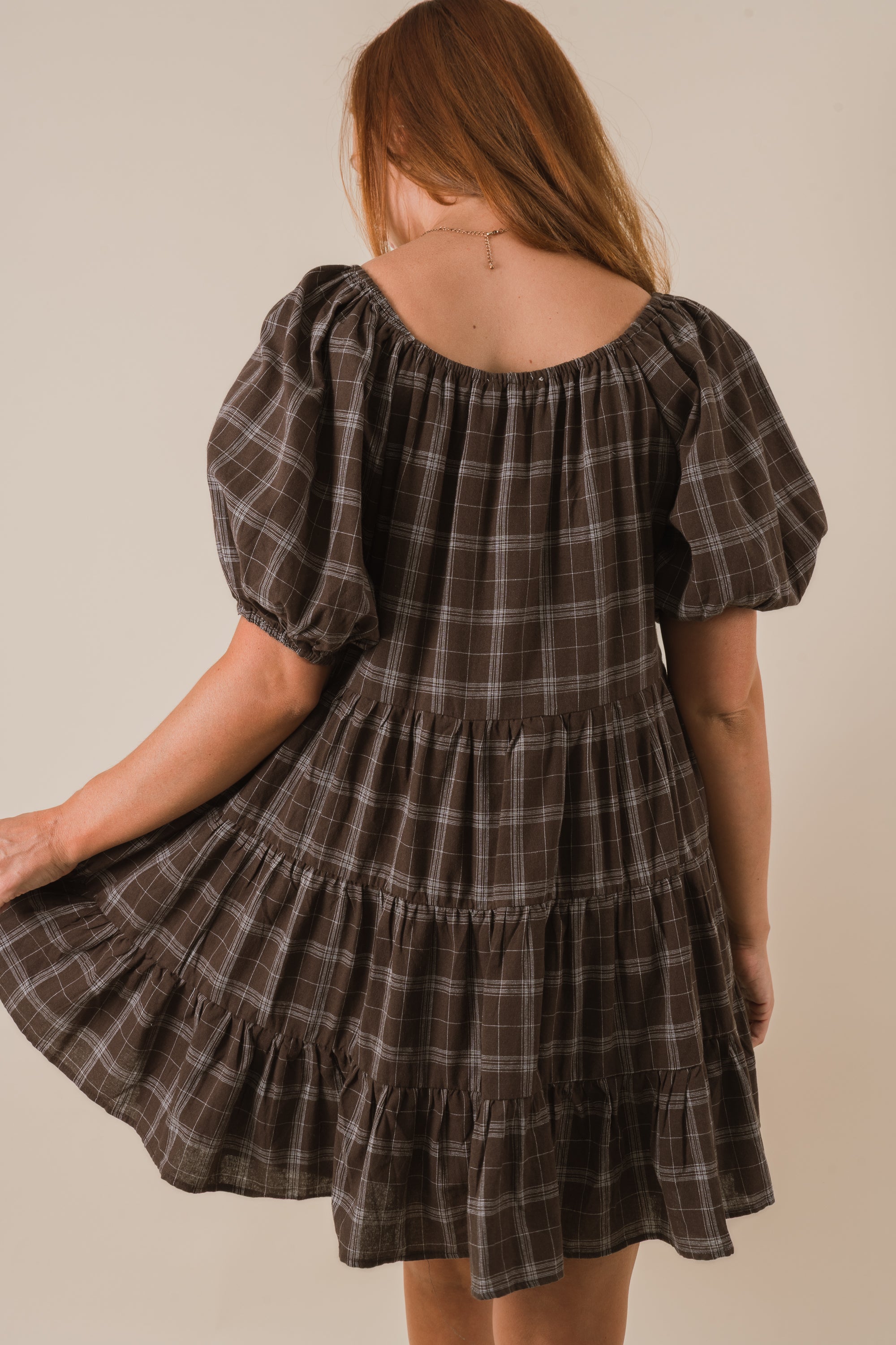 Woman wearing a plaid dress with puff sleeves on a neutral background