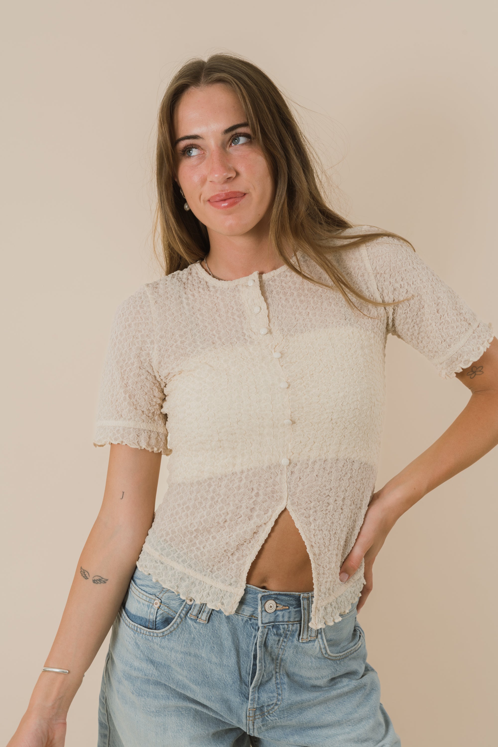 Woman wearing a beige textured top and blue jeans against a beige background