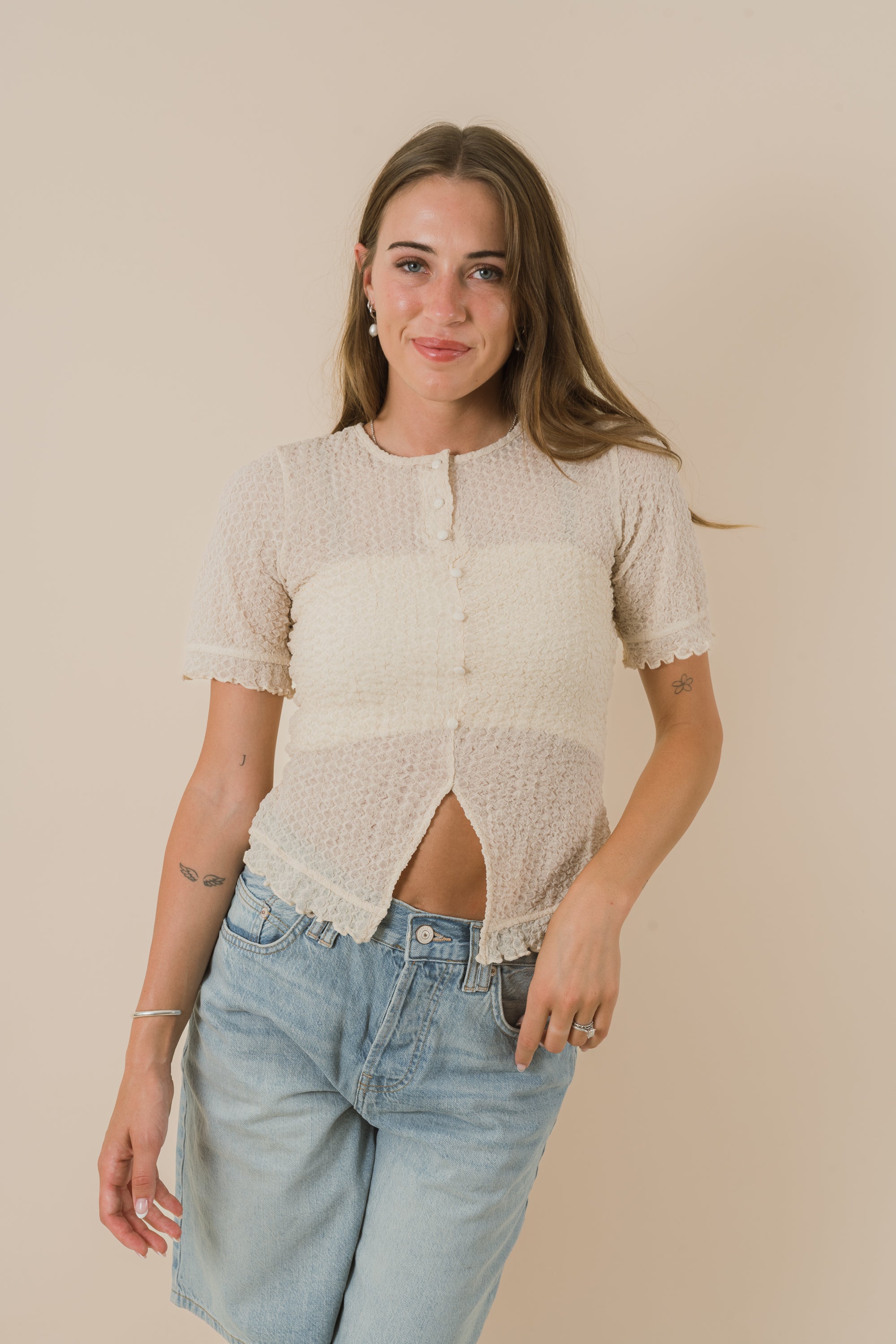 Woman wearing a beige short-sleeve top and light blue jeans against a beige background