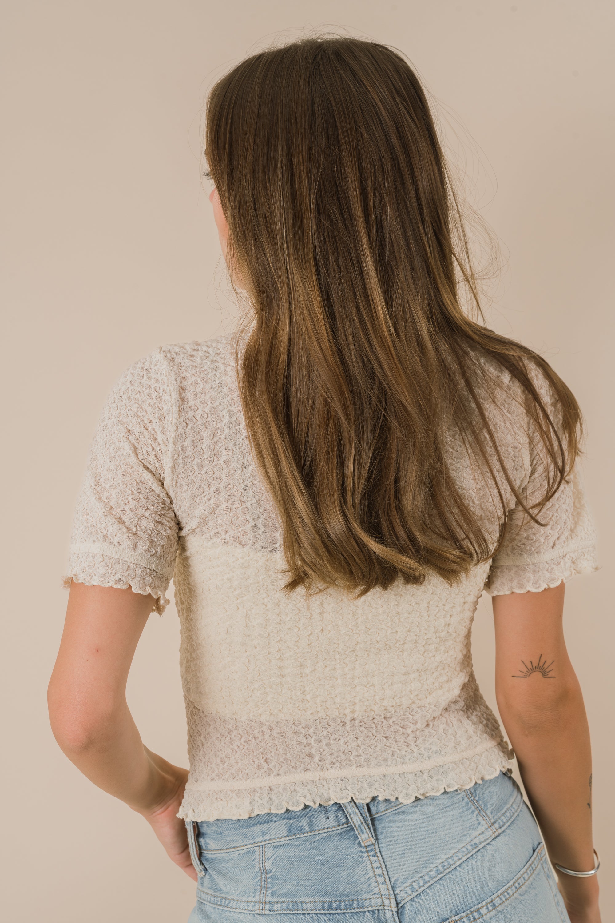 Woman wearing a light-colored sheer top and blue jeans against a beige background
