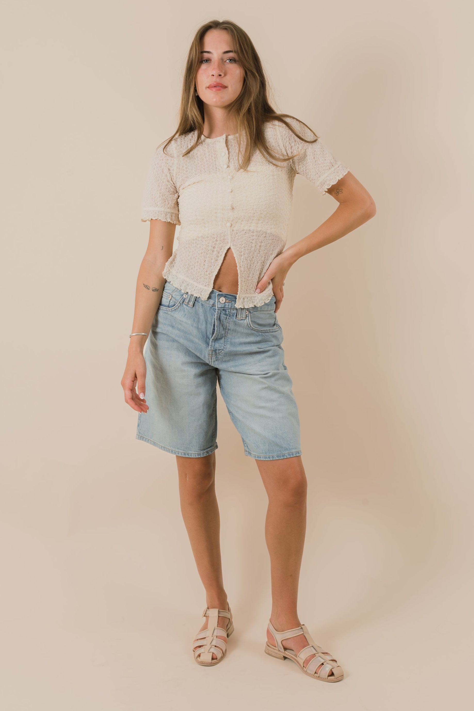 Woman wearing a beige top and light blue denim shorts against a beige background