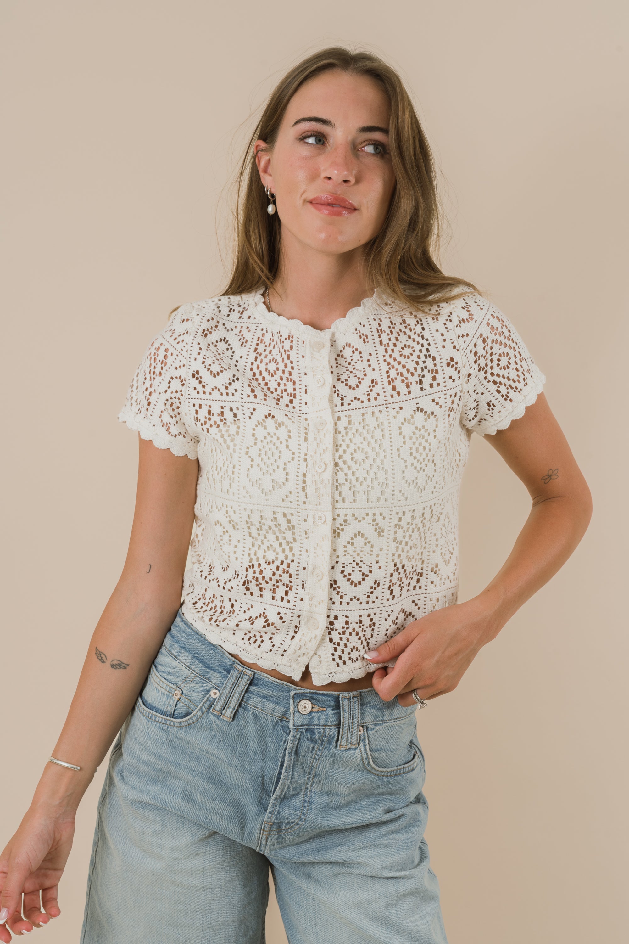 Woman wearing a white lace top and light blue jeans against a beige background