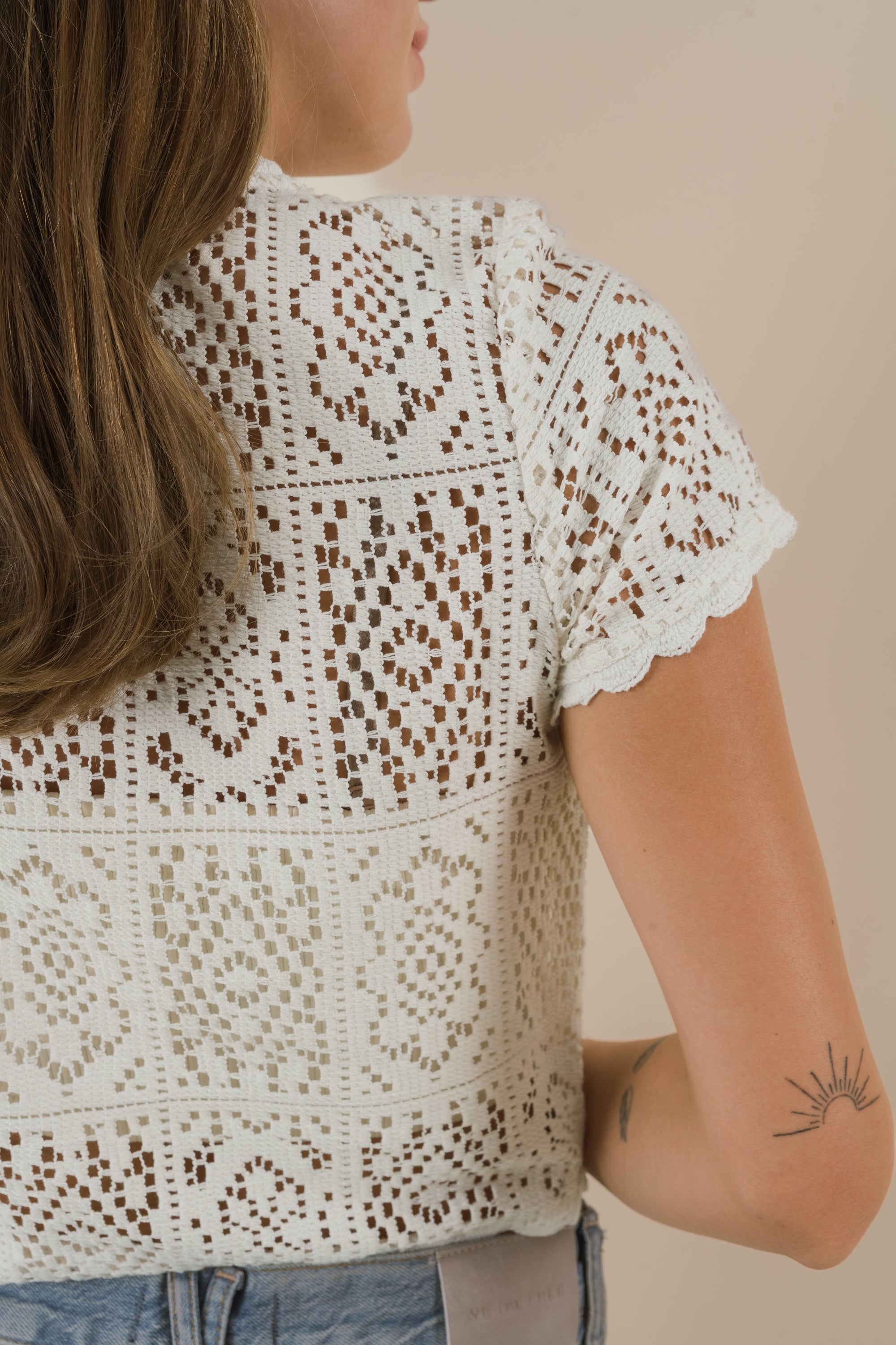 Woman wearing a white lace top against a beige background