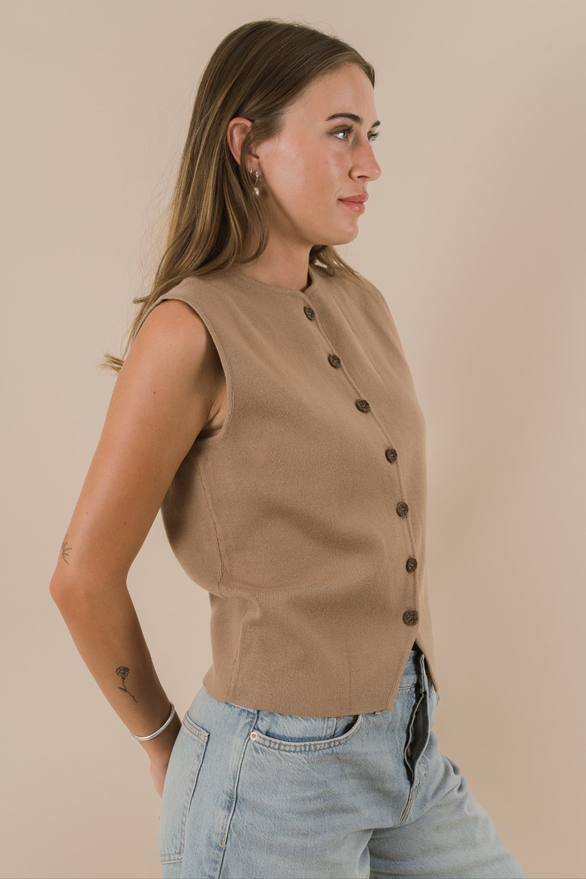 Woman wearing a beige sleeveless top with buttons against a beige background