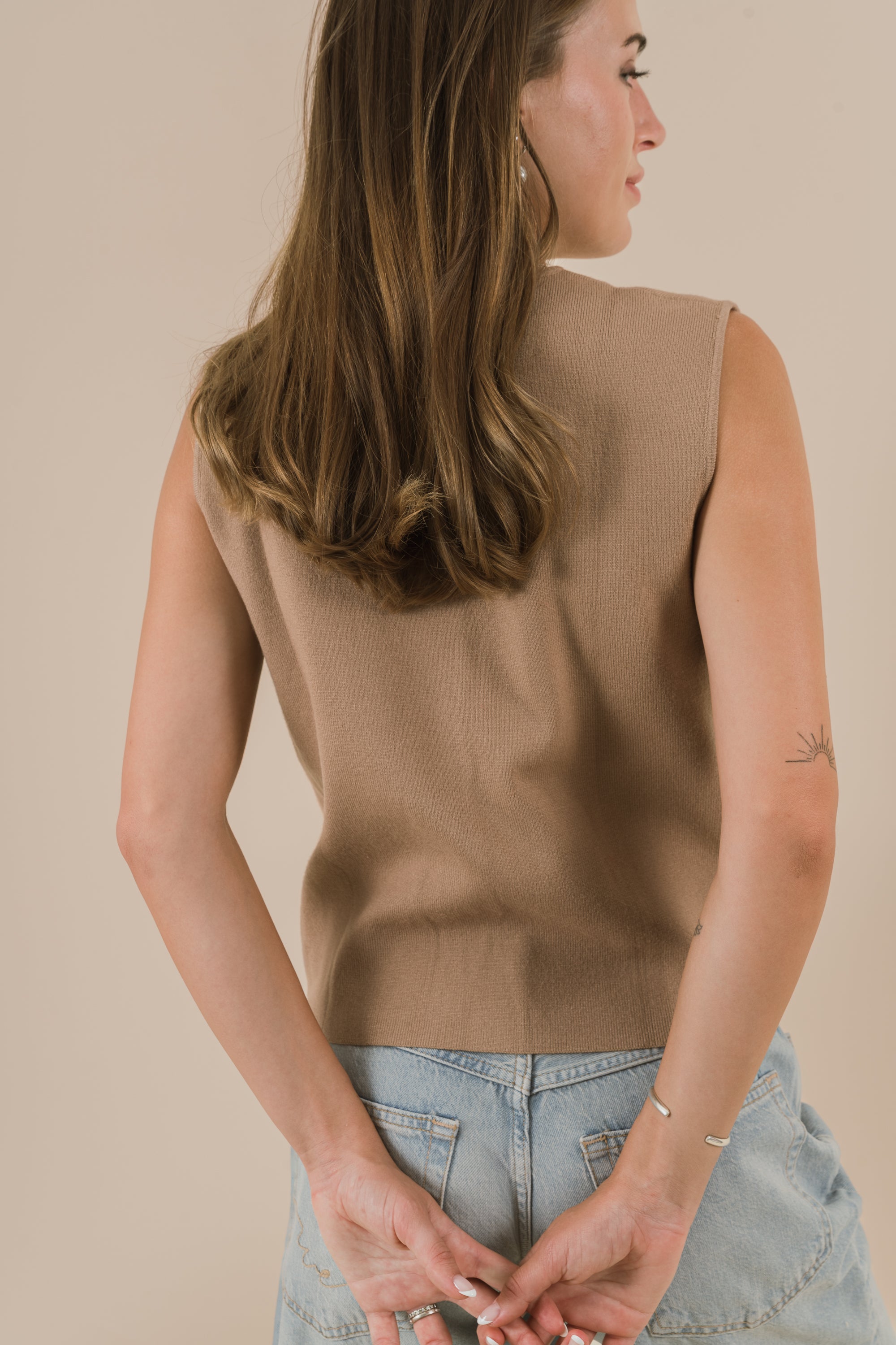 Woman wearing a brown sleeveless top and blue jeans against a beige background