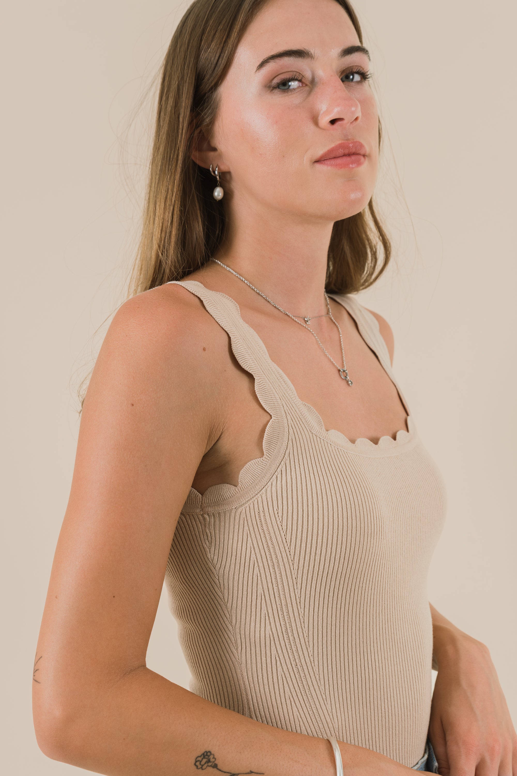 Woman wearing a beige ribbed tank top against a plain background